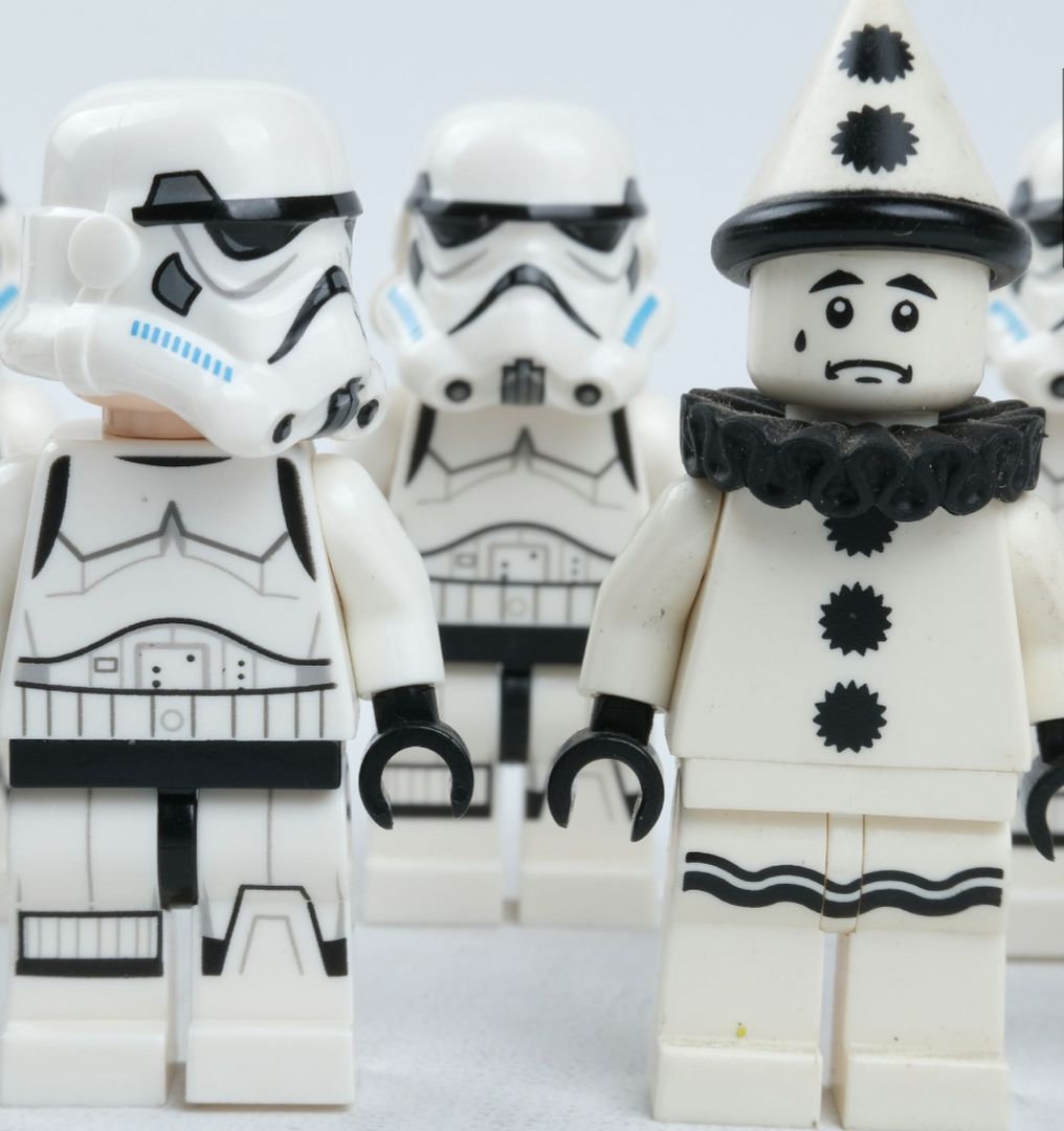 Close-up of LEGO minifigures including three stormtroopers and one clown with a white face, black ruffled collar, and a cone-shaped hat with black spots.