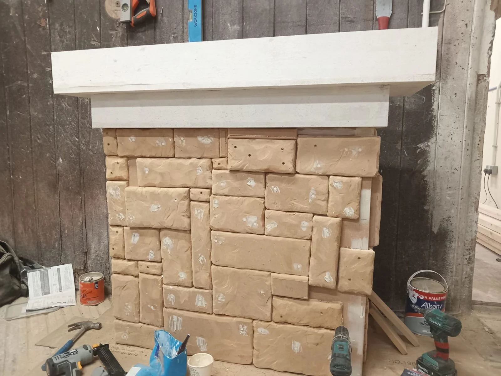 Construction site with a wall made of beige stone bricks in progress, with tools and construction materials scattered around.