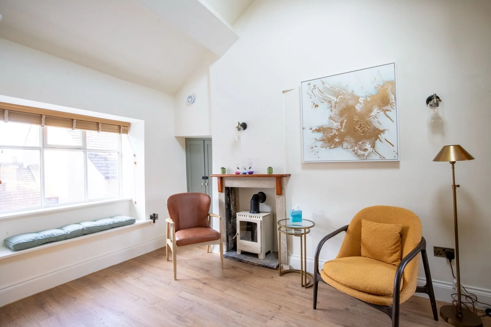 Living room with a large window, a brown and yellow armchair, a small fireplace, and abstract artwork on the wall.