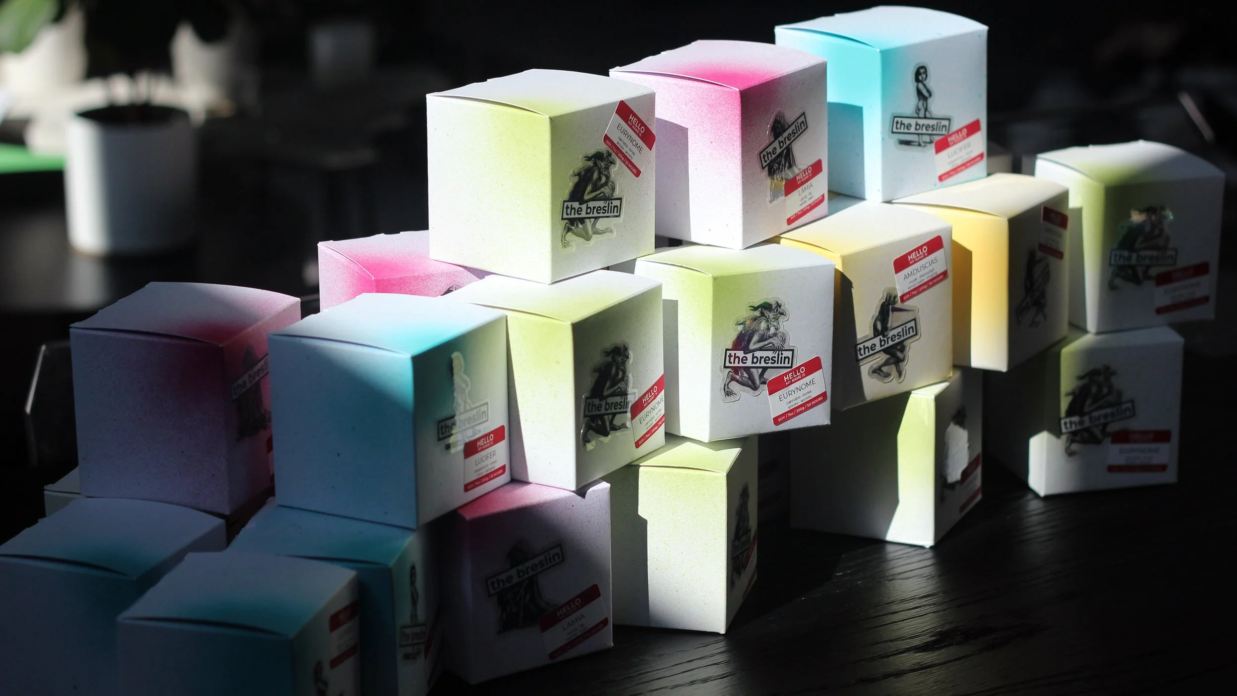 Colorful boxes with stickers and labels stacked on a dark surface, some boxes have light pastel colors like pink, blue, and green.