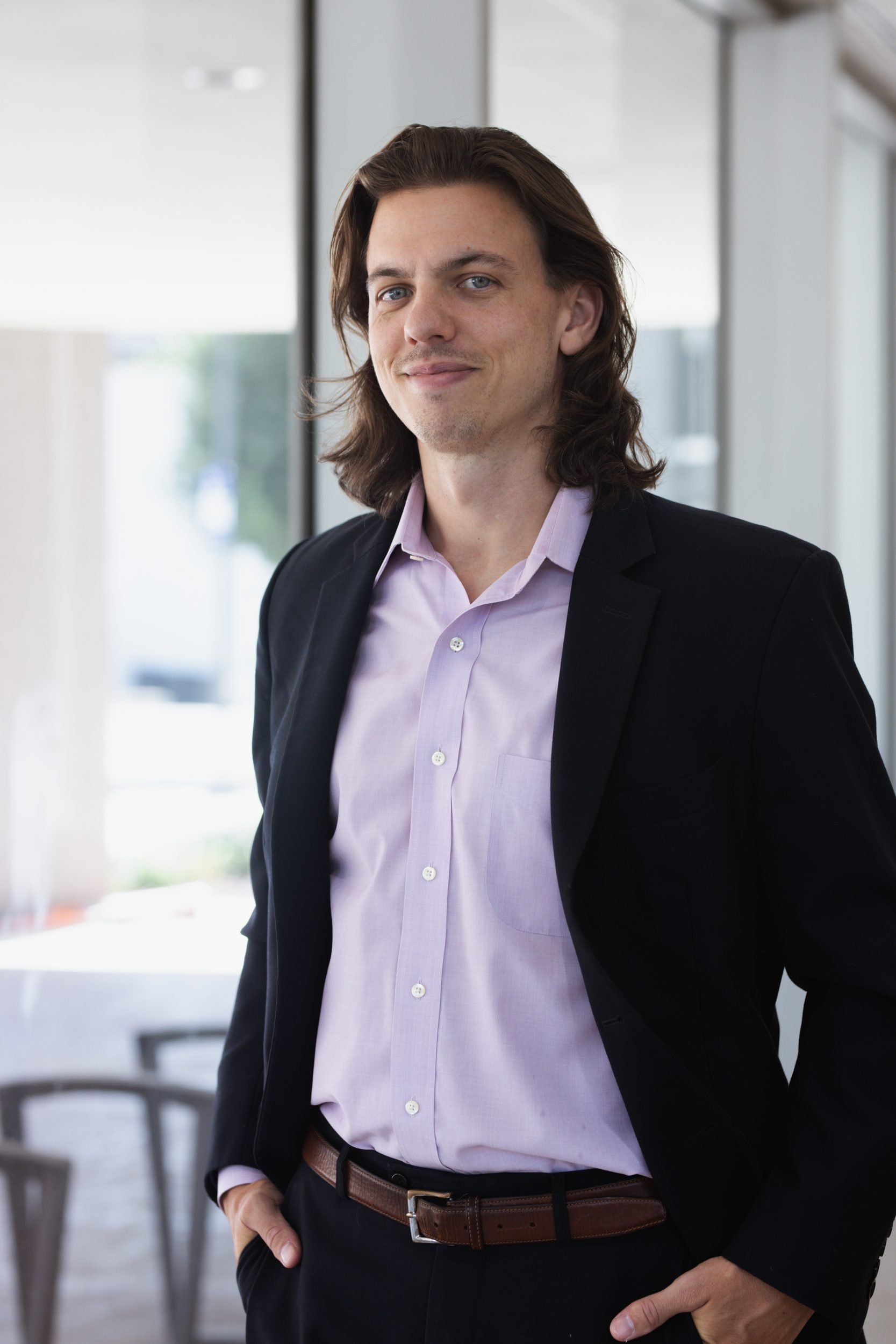 Will Oldfather in a dark blazer, standing in a modern office with a slight smile