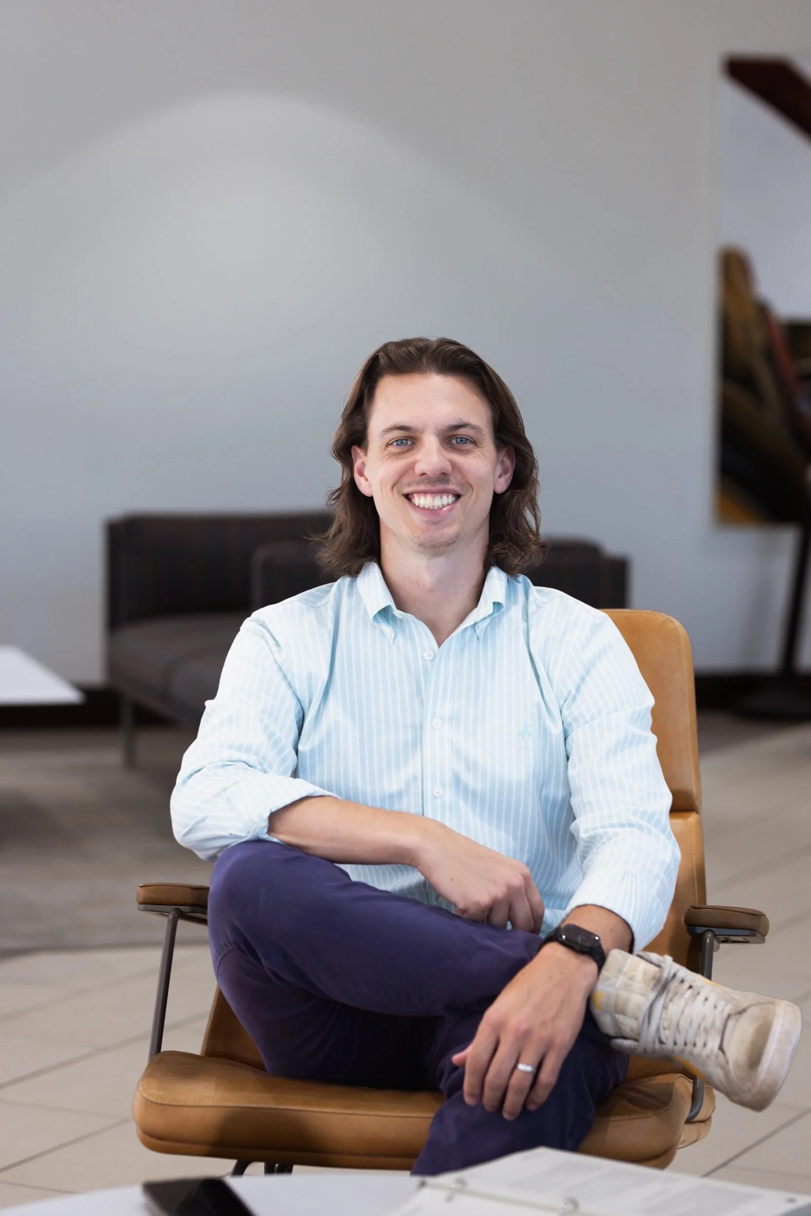 Will Oldfather, leadership and career coach, smiling and seated in a leather chair in a bright office