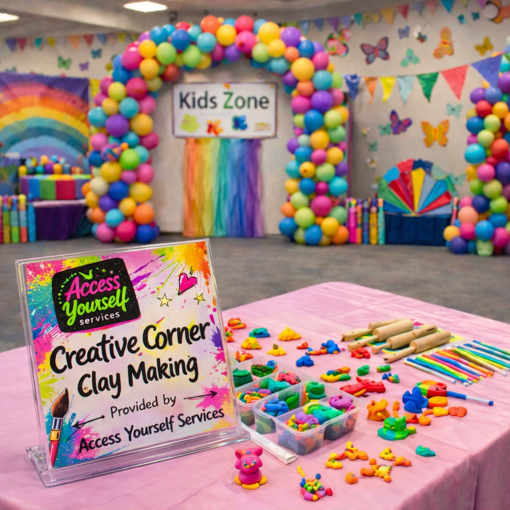 Colorful balloon arch and kids' craft area with clay making station, sign reading 'Access Yourself Creative Corner Clay Making' at a children's event, decorated with rainbow and butterfly themes.