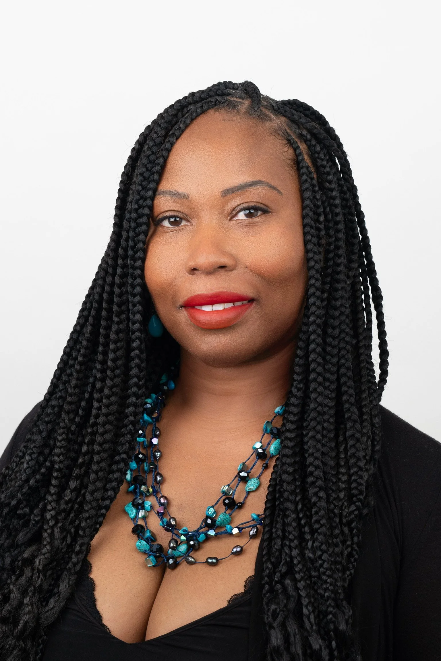Professional headshot of Jasmin Todd, licensed trichologist and educator, wearing a black top and blue statement necklace on a white background