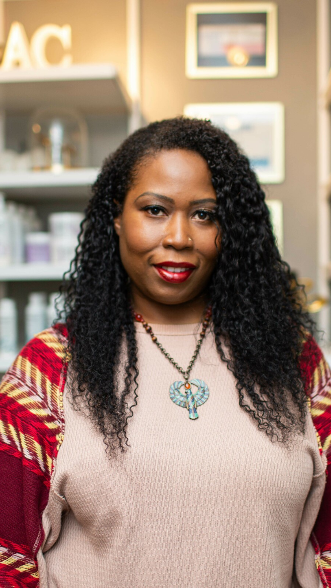 Jasmin Todd, curl coach and author, smiling outdoors in a bright blue coat with natural curls, seated on a green chair
