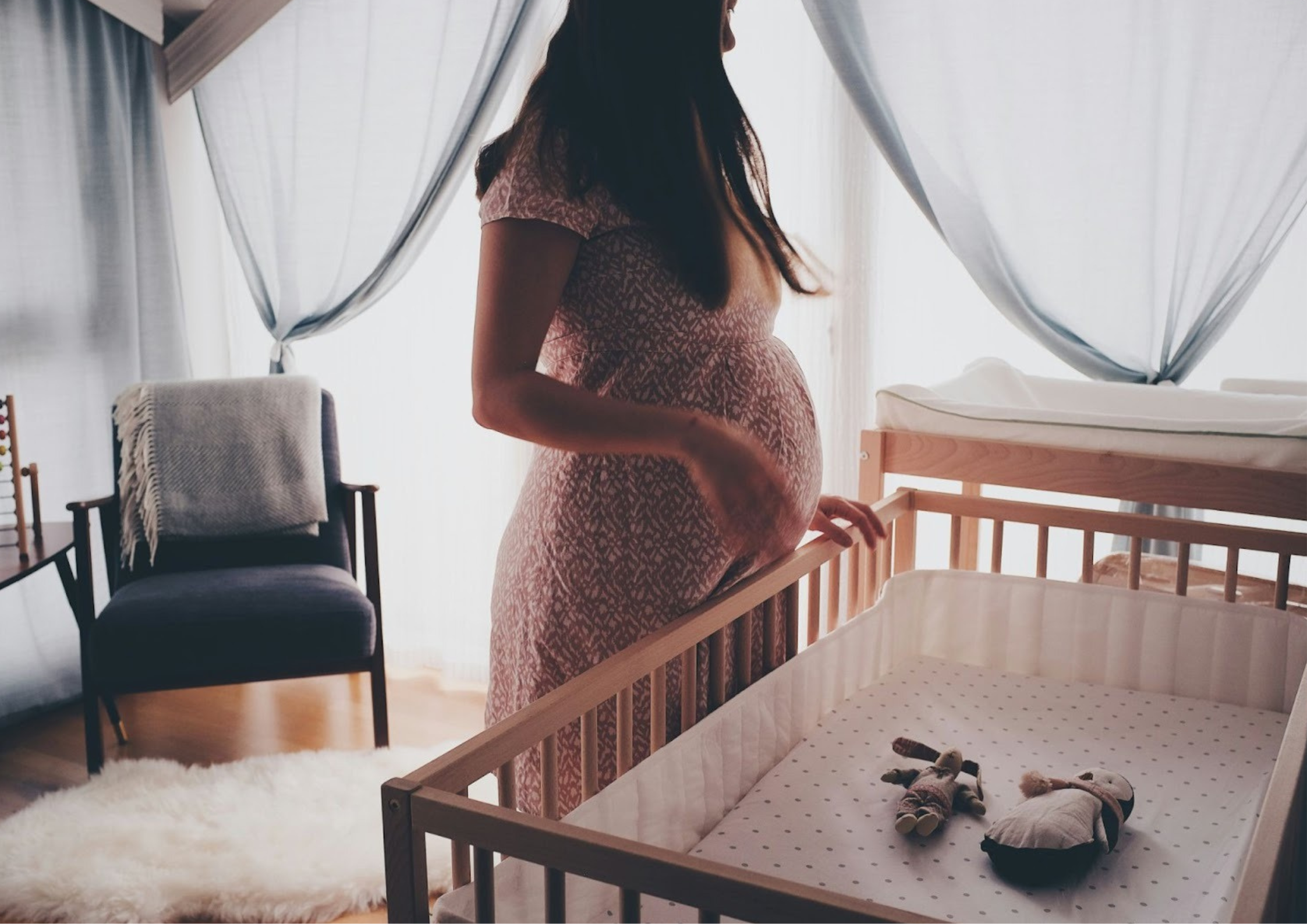 A pregnant woman standing beside a crib in a softly lit nursery, capturing the anxiety and anticipation often felt during post traumatic stress in pregnancy. - Whole Mother Story
