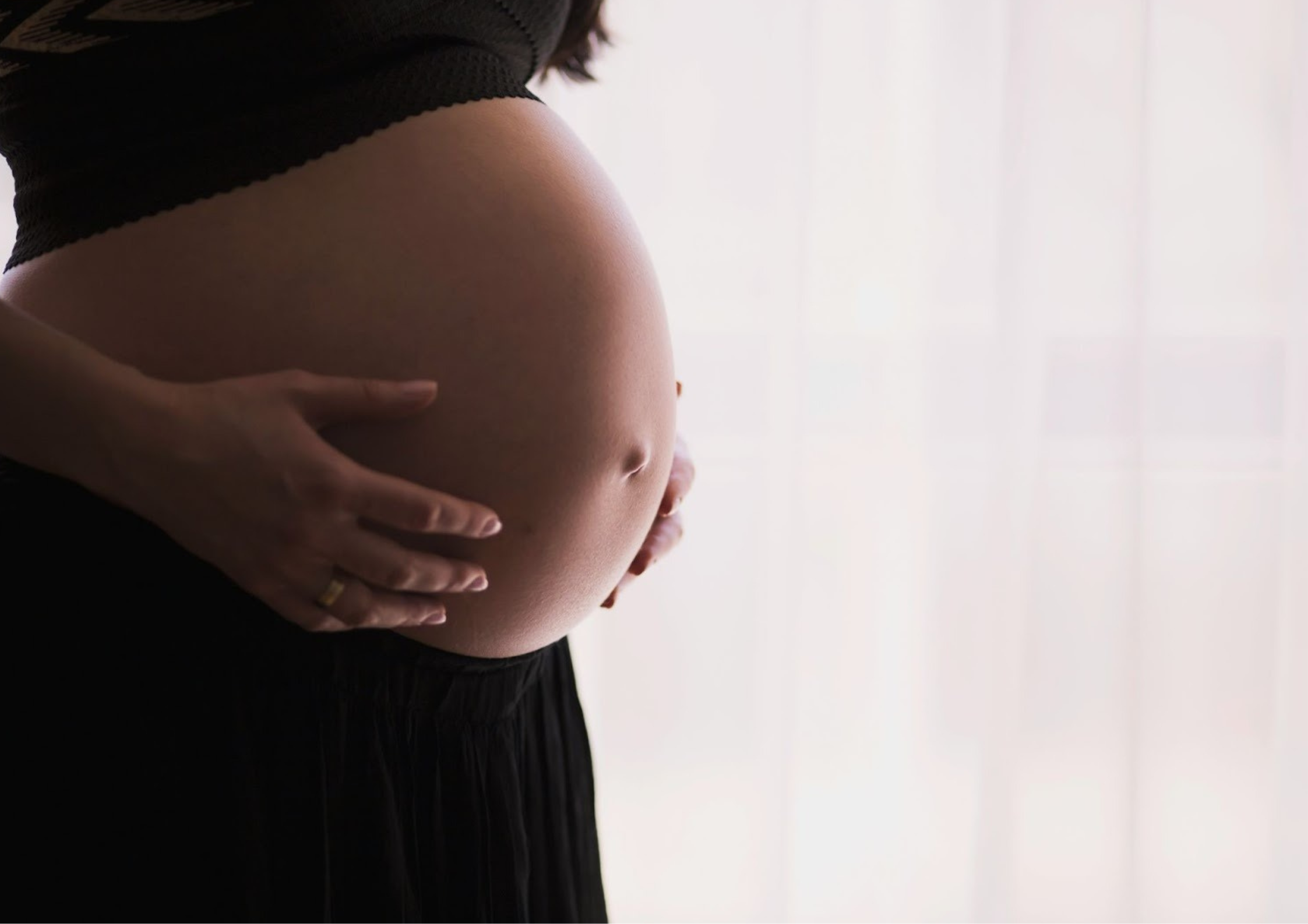 A close-up of a pregnant belly held gently with both hands, illustrating the vulnerability and emotional weight of post traumatic stress in pregnancy. - Whole Mother Story