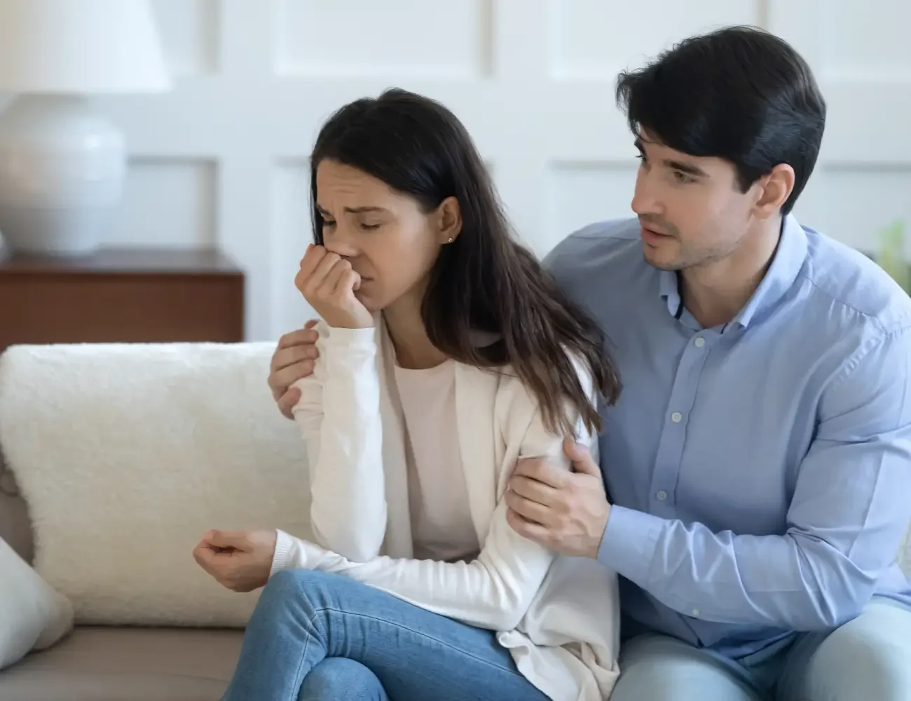 A man and woman sit together on a couch, holding hands and sharing a moment of connection.