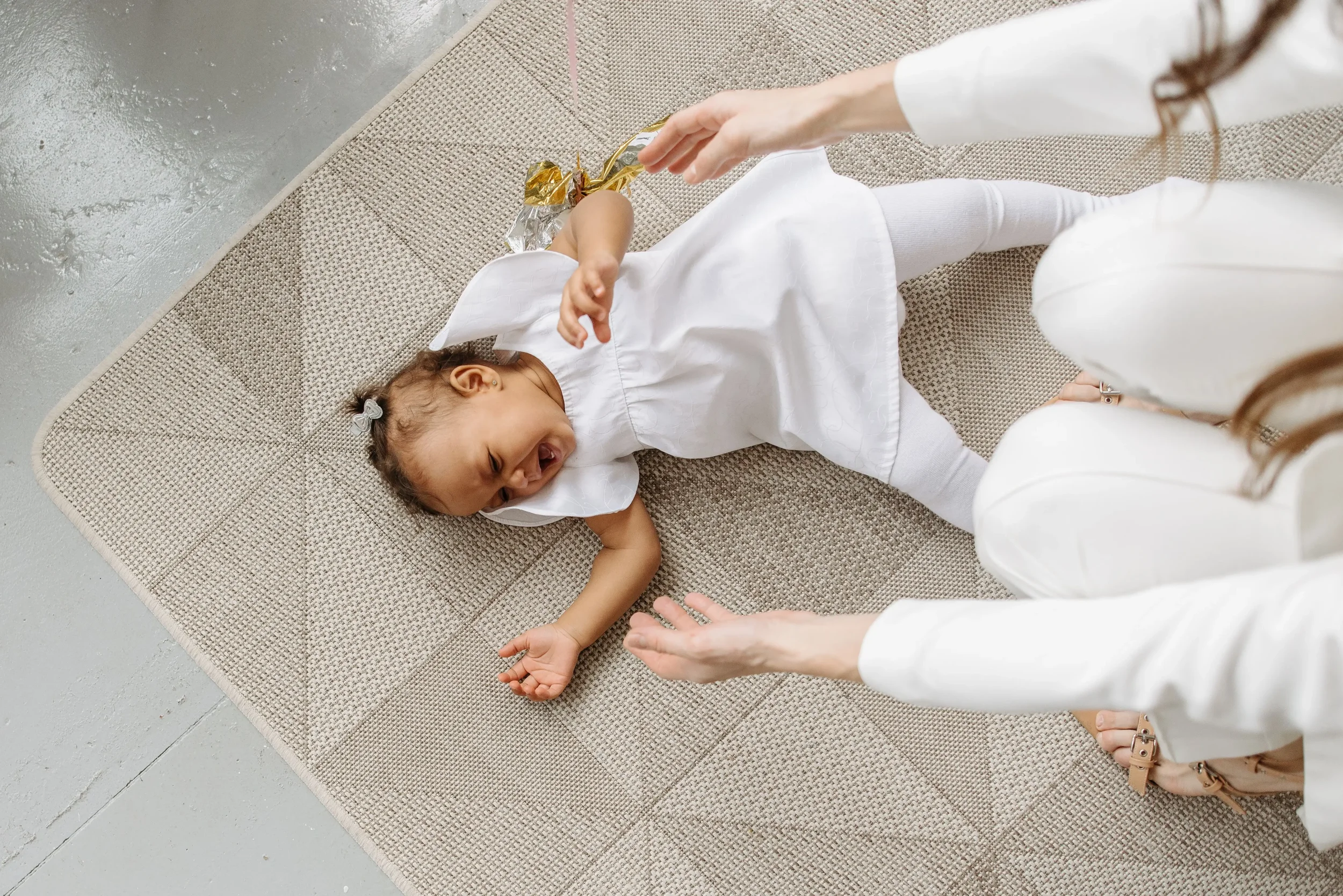 Mother reaching toward her crying baby on a rug, reflecting the overwhelm and emotional strain associated with postpartum rage.