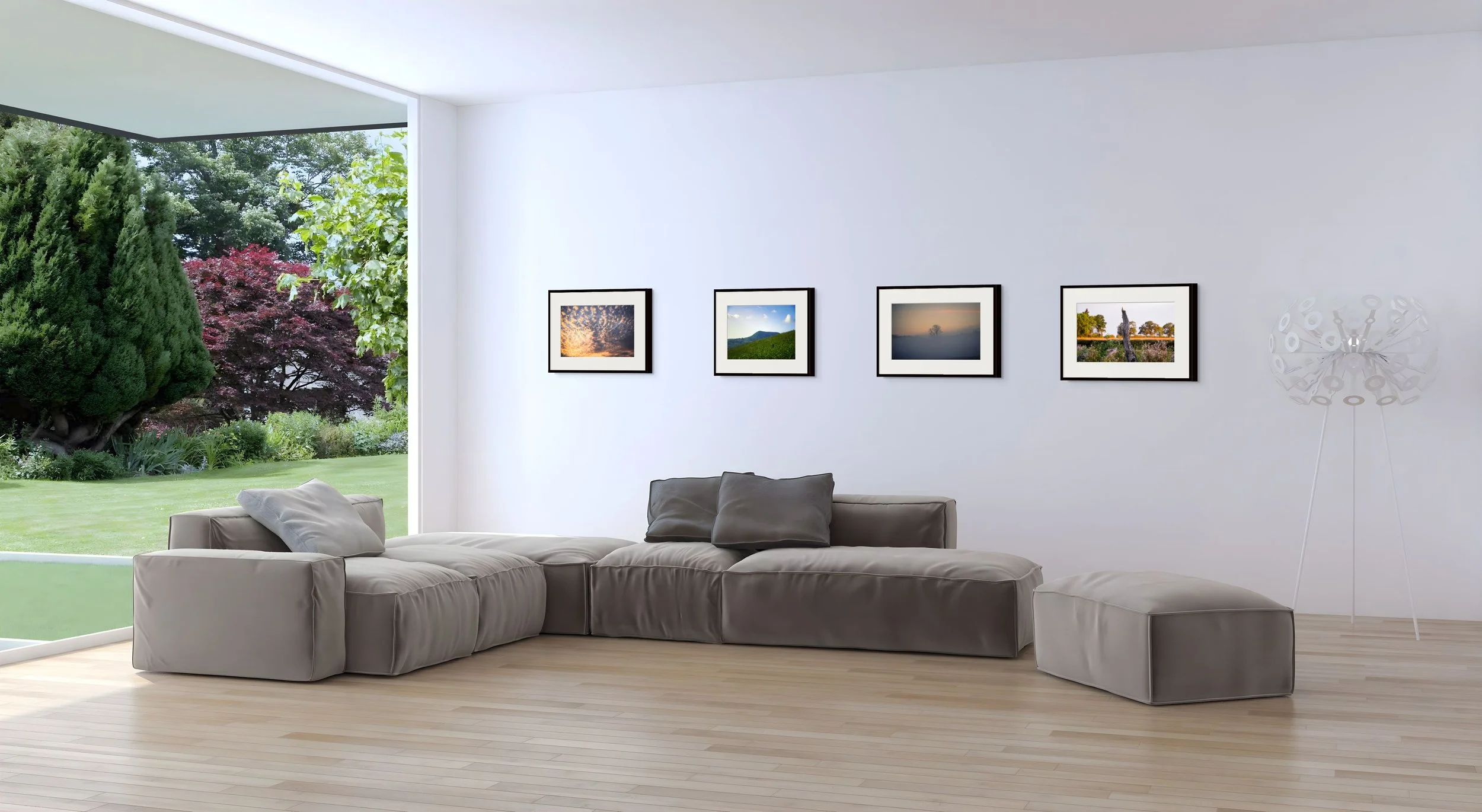 Bright living room with gray sectional sofa, landscape photo gallery, and garden views through a large window and airy interior.