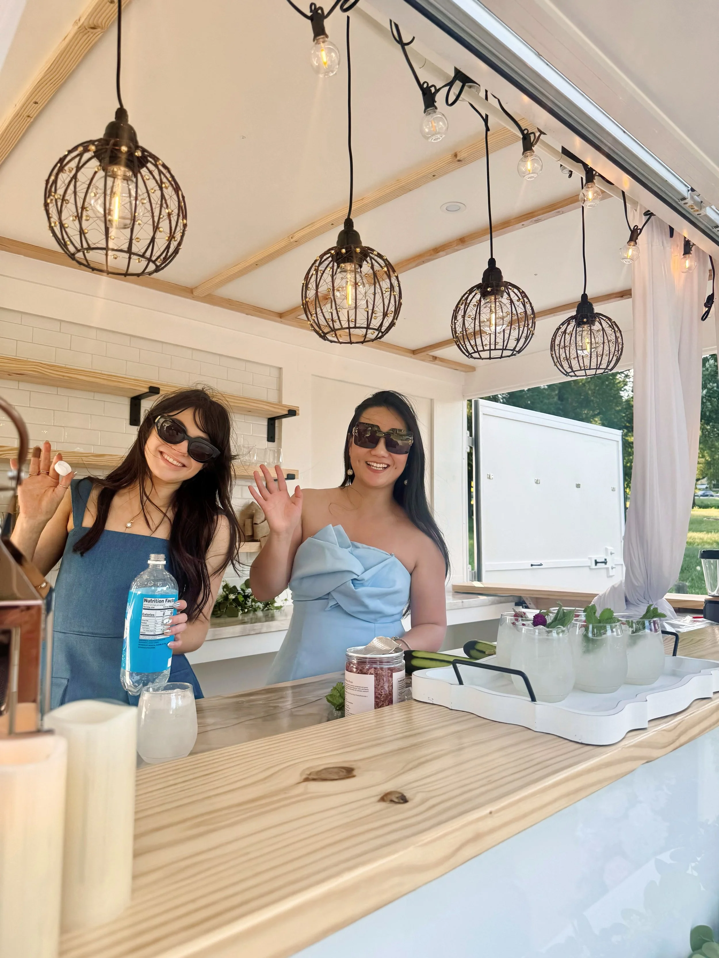 Lumière Bubble Co. owner and bartender welcoming guests beside a tray of signature cocktails inside the luxury mobile bar trailer at a Dallas-Fort Worth event.