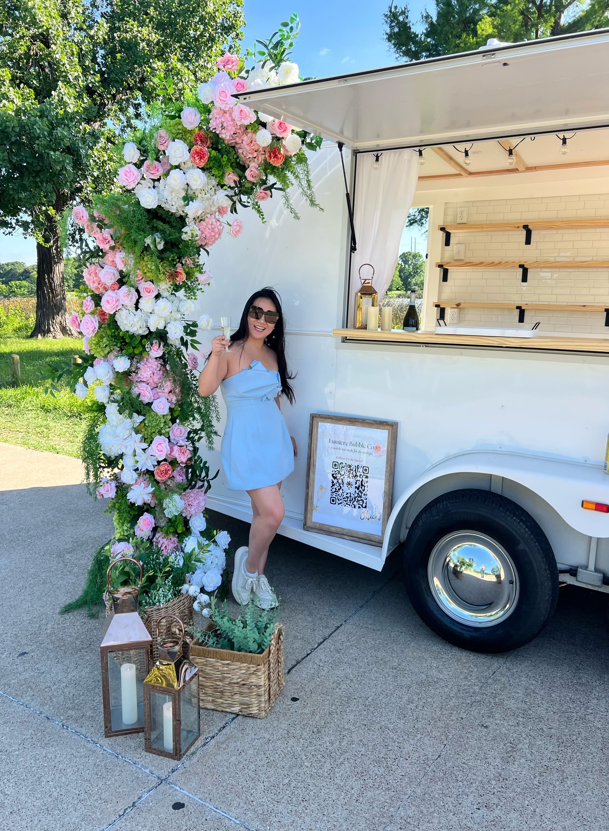Lumière Bubble Co.'s owner celebrating with a glass of champagne beside the luxury mobile bar at an outdoor Dallas-Fort Worth event.