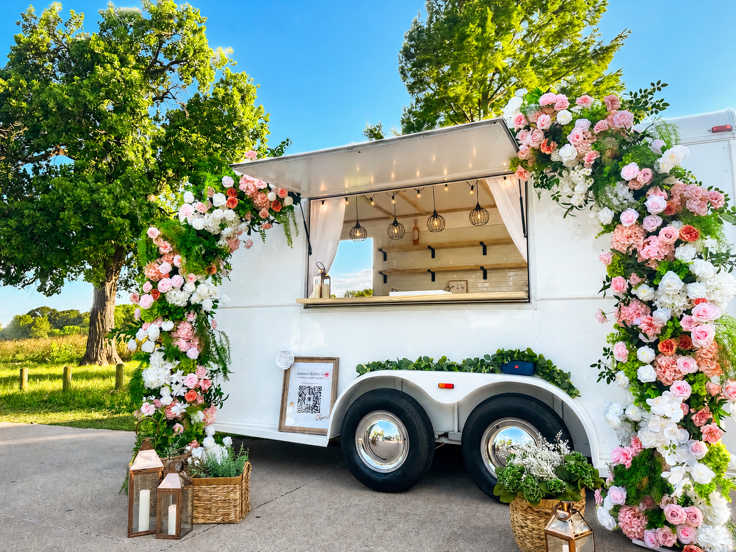 Lumière Bubble Co.'s white mobile bar trailer framed with pink-and-white florals at an outdoor Dallas-Fort Worth event.