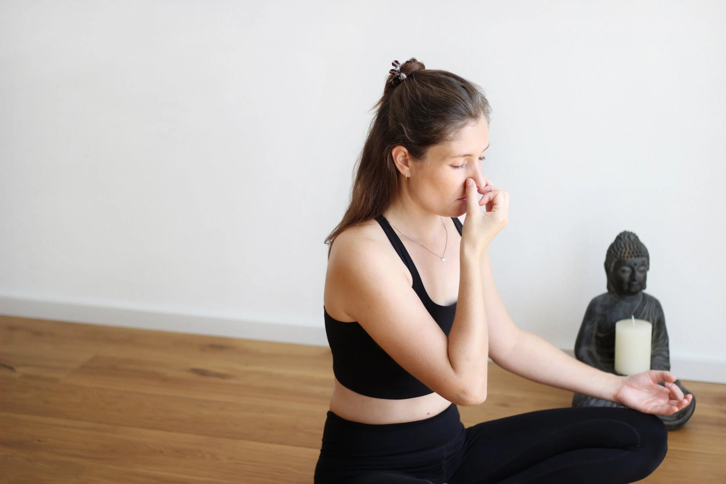Frau meditiert bei einer Atemübung im Yogasaal in Kaufbeuren neben Buddha-Statue mit Kerze.