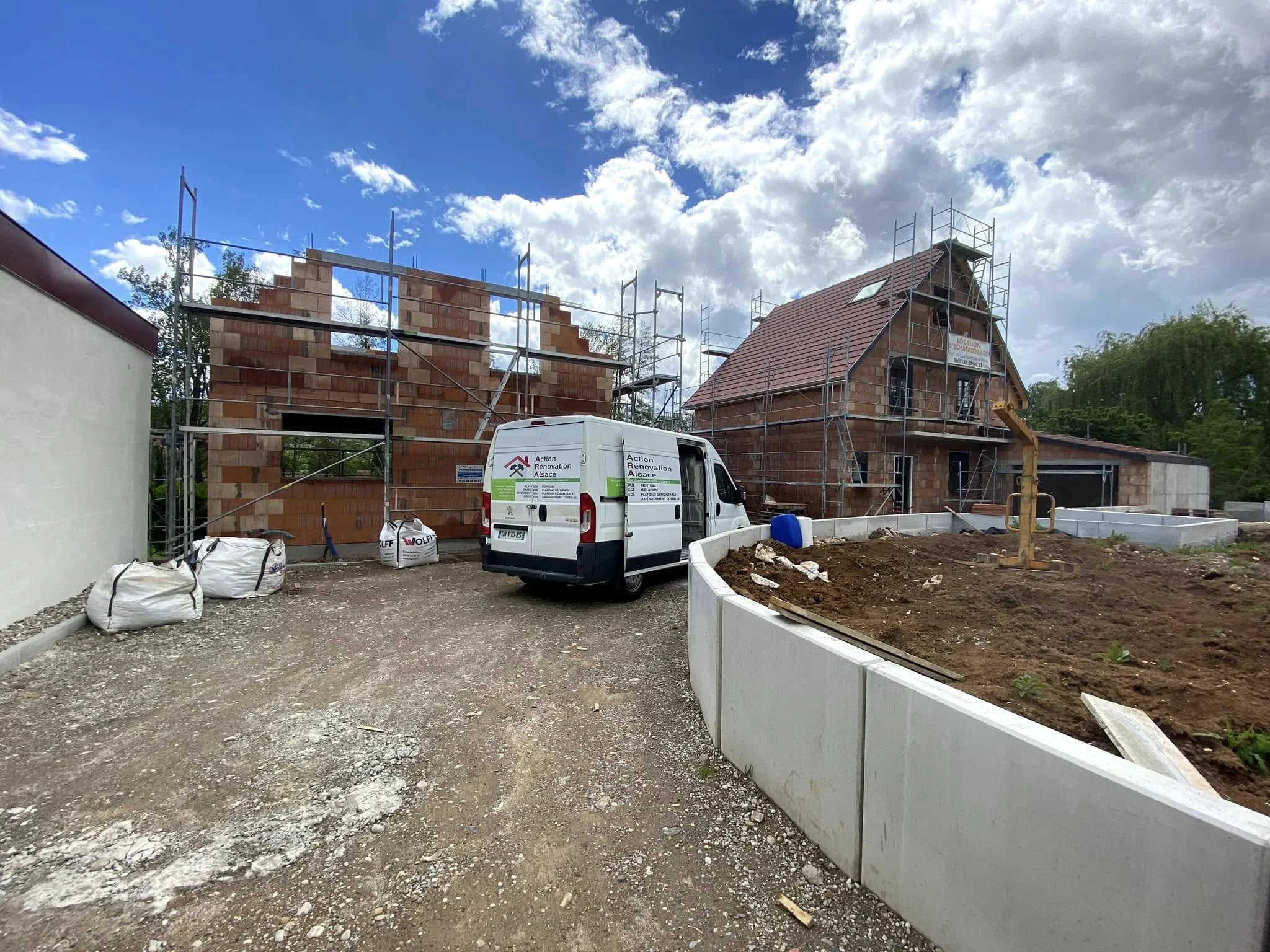 Construction d'une maison avec scaffolding, un véhicule de service, terrain en terra formation et matériaux de construction.