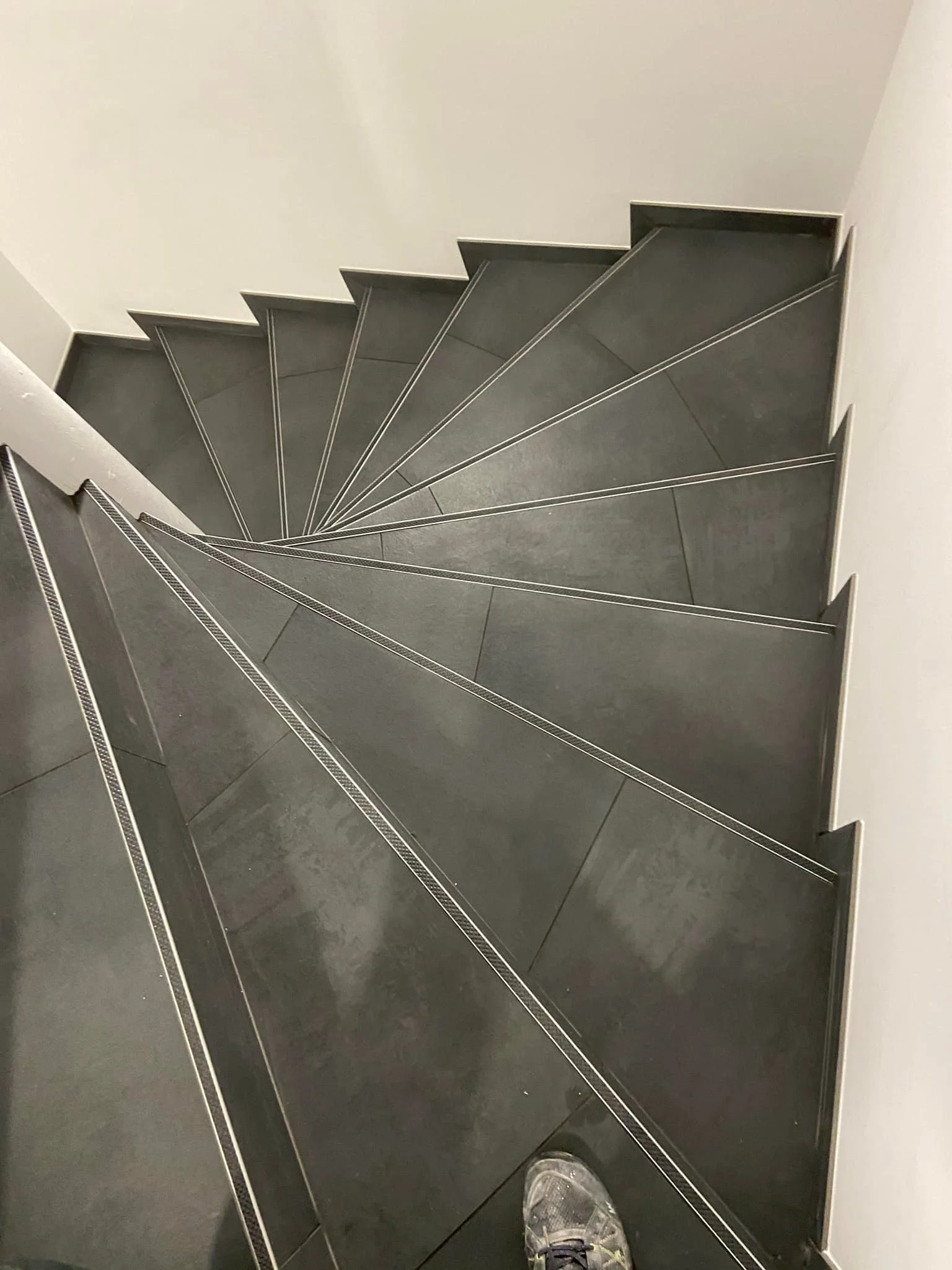 Escalier en acier avec marches en gris foncé, vus du haut vers le bas, avec un pied en chaussure visible à l'avant.