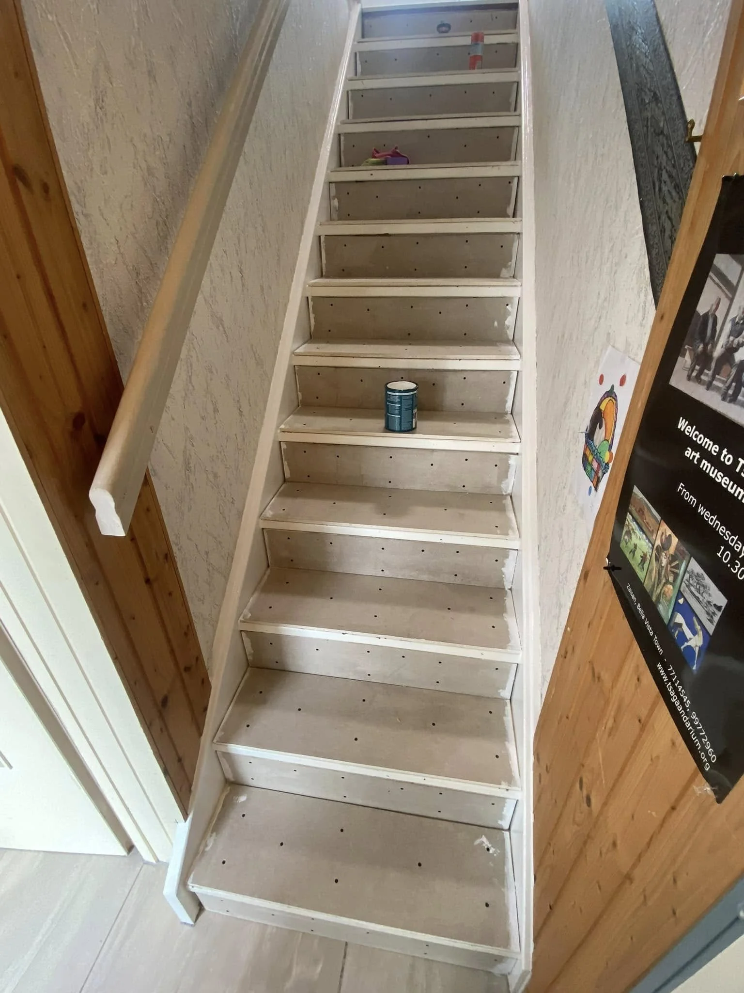 Escabeau en bois en cours de peinture dans une maison, avec une peinture en haut de l'escalier et un pot de peinture posé sur la marche du milieu.