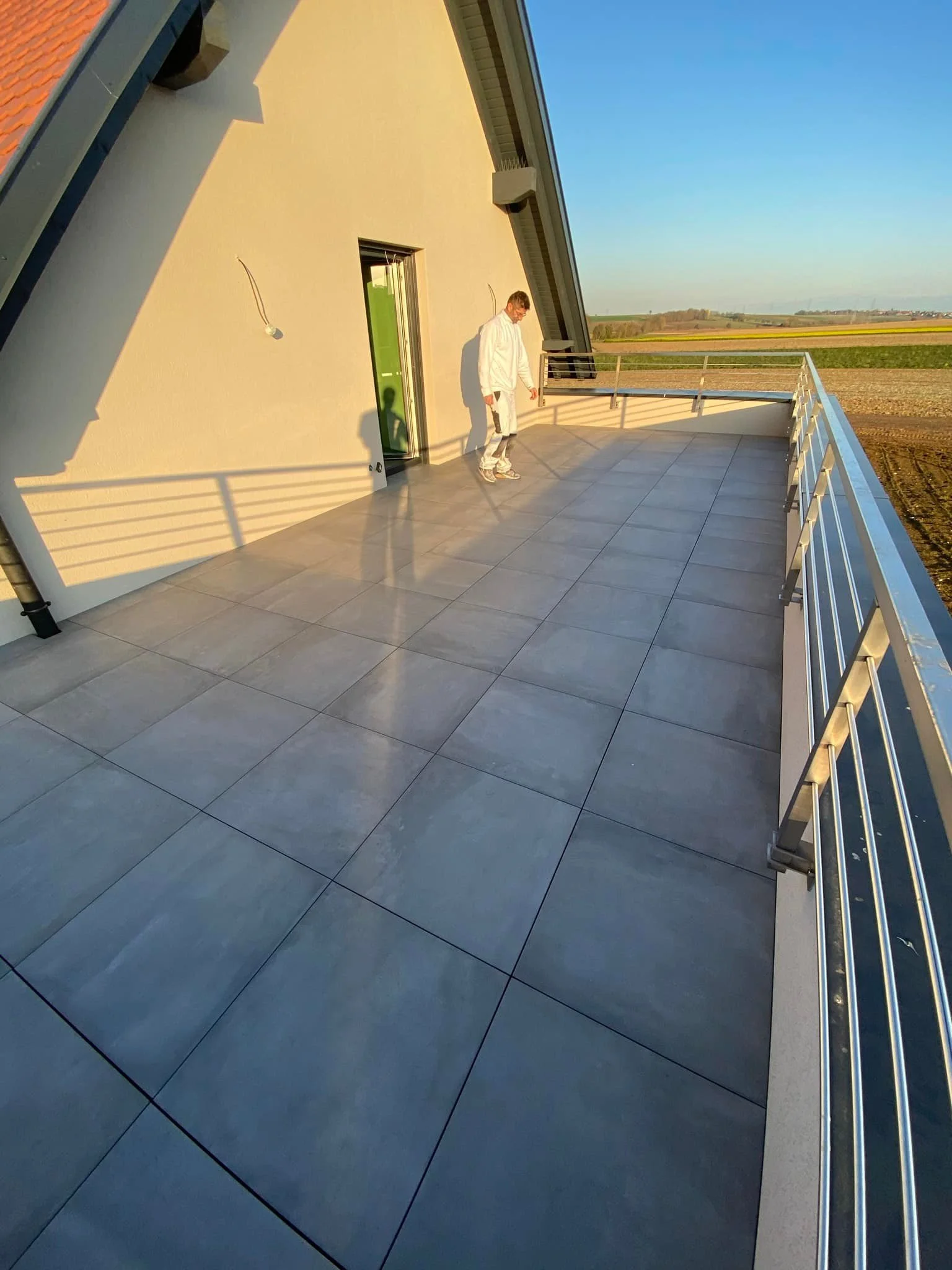Balcon ensoleillé avec un homme habillé en blanc signant la lumière du soleil, vue sur des champs agricoles au loin.