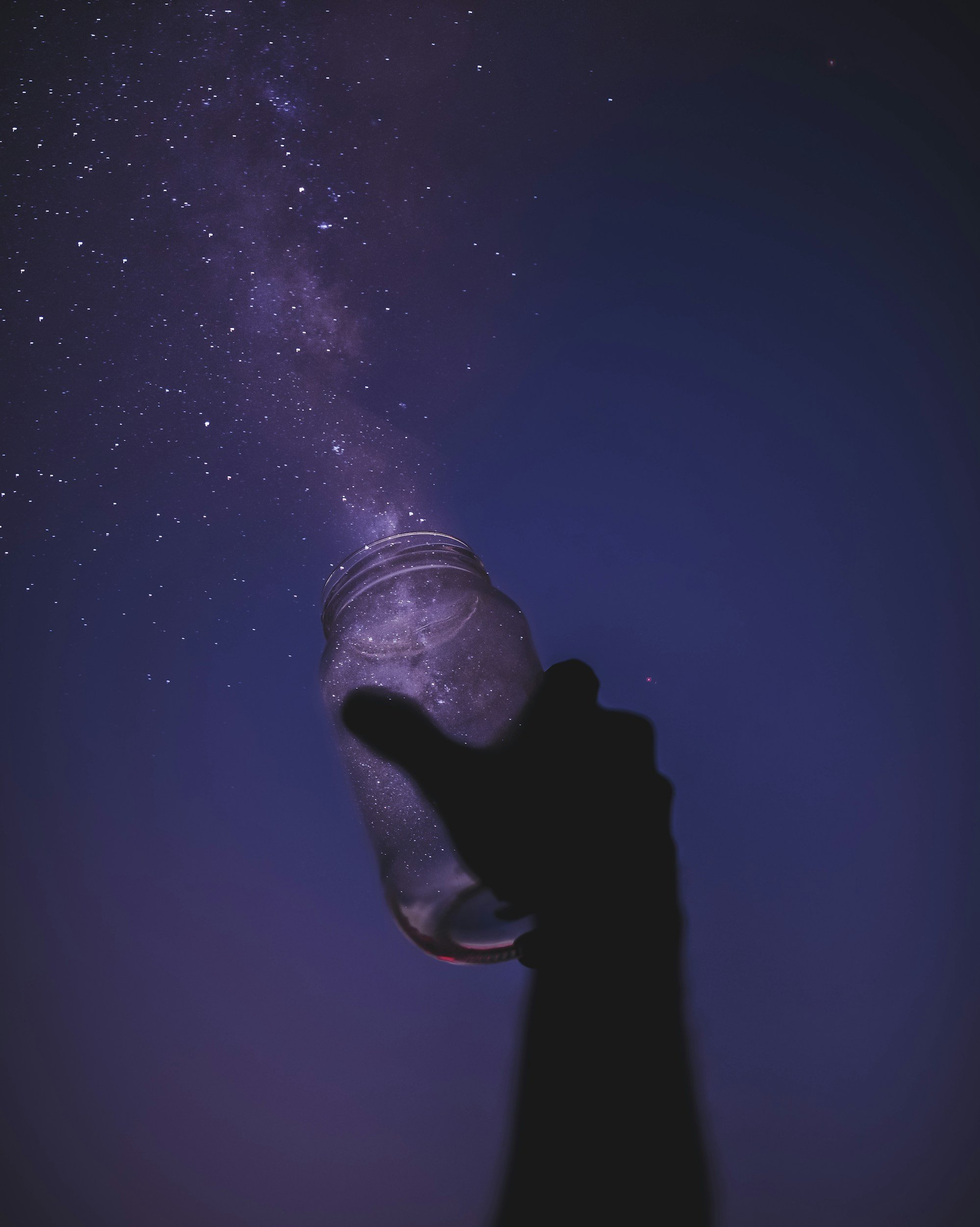 Silhouette of a person holding a jar under a starry night sky with the Milky Way galaxy visible.
