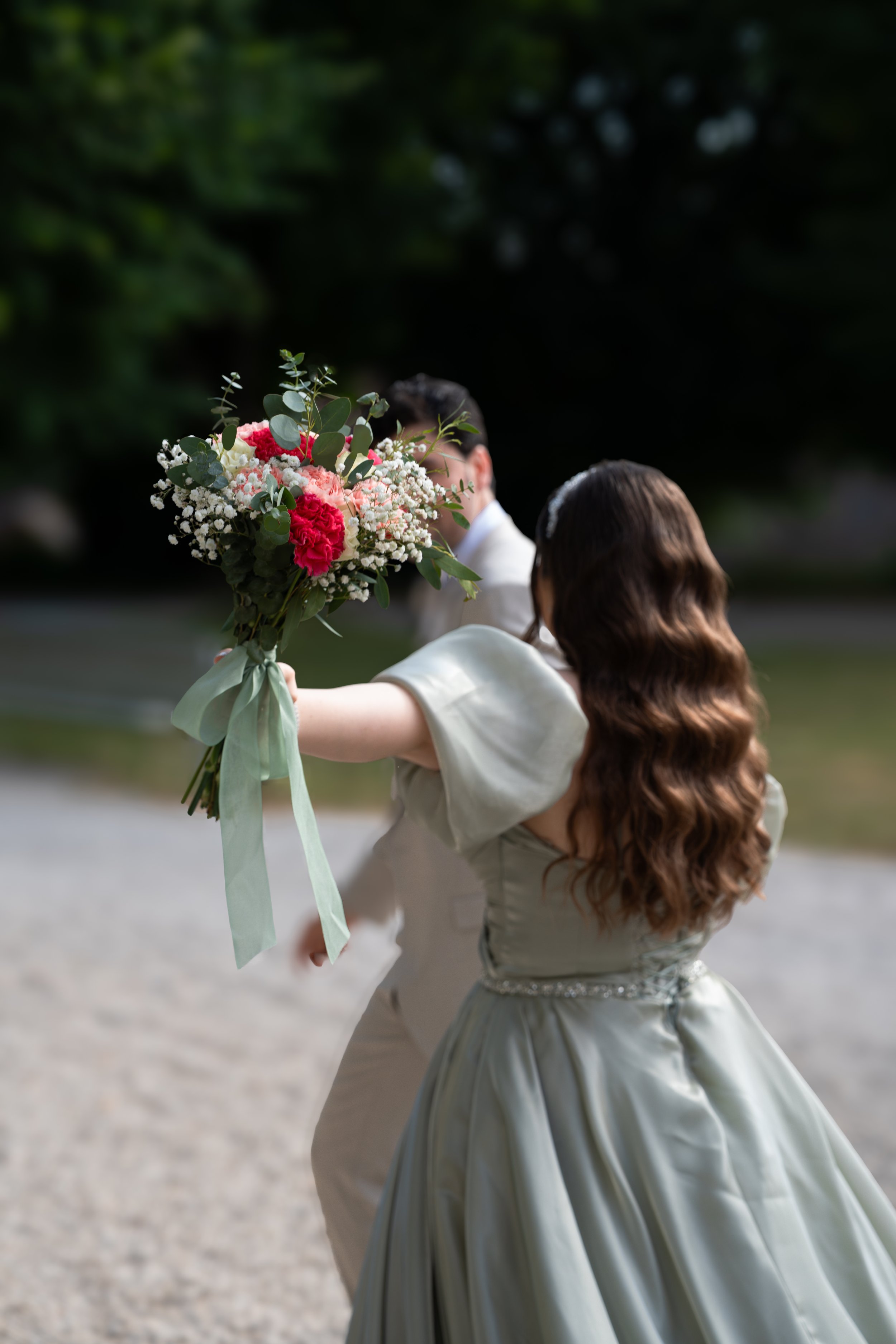 Ein Brautpaar bei einer Hochzeit, die Braut hält einen großen Blumenstrauß mit rosa, weißen Blumen und grünen Blättern in der Hand.