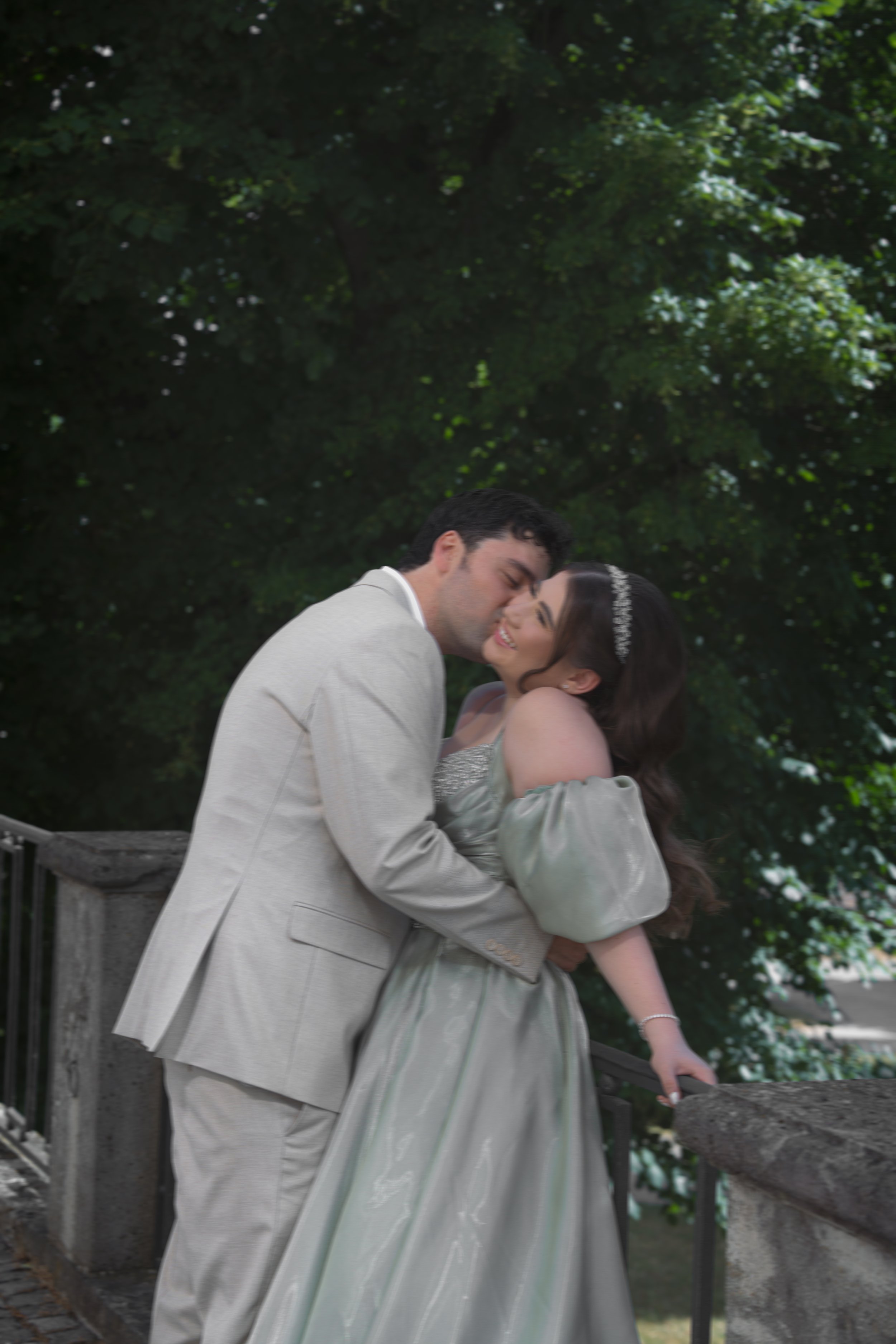 Ein Paar bei einer Hochzeitsfeier, umarmt und lacht, vor einem Baum.