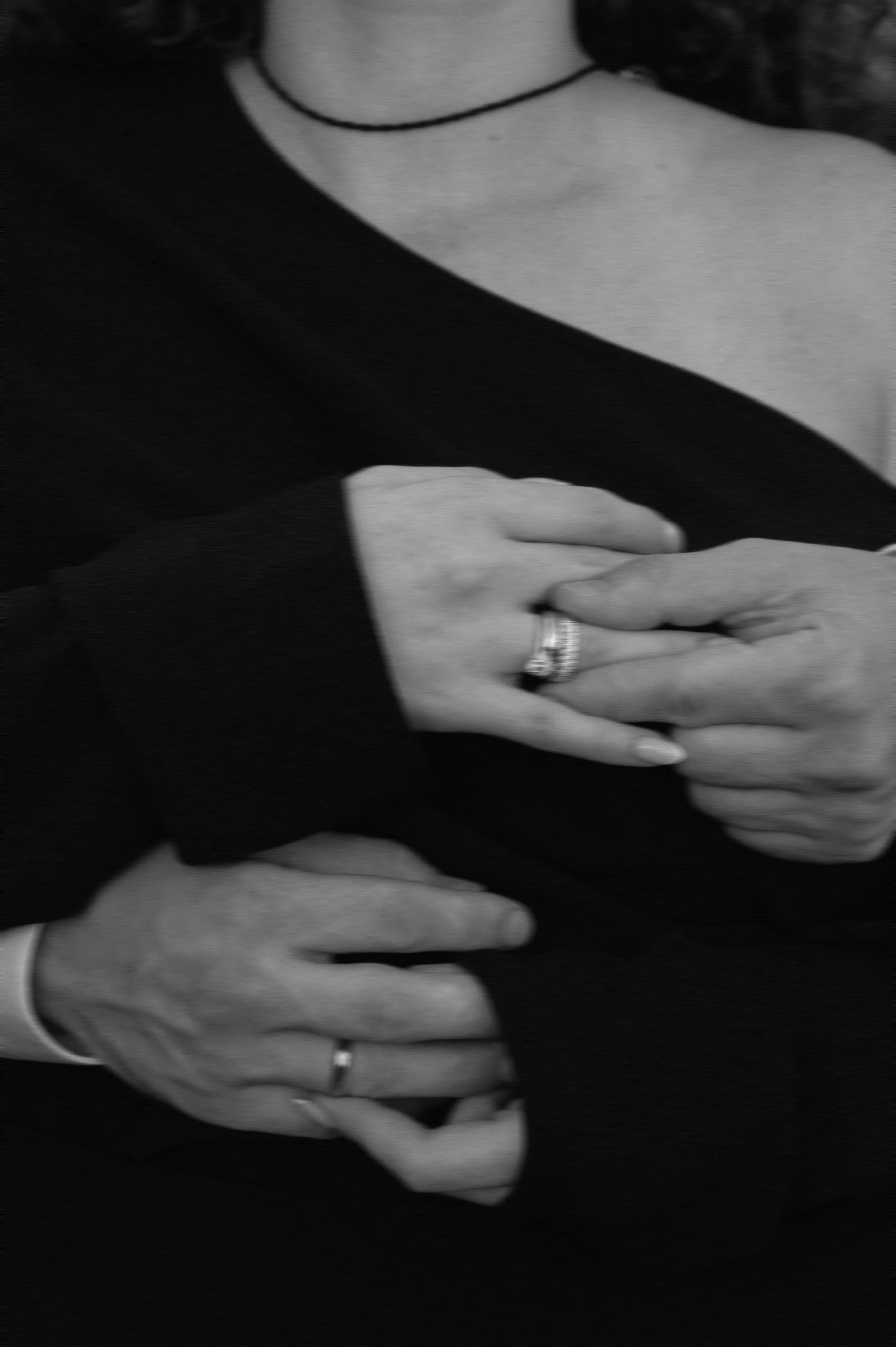 Nahaufnahme von Händen, die sich berühren, mit Eheringen, auf einem schwarzen Kleid.