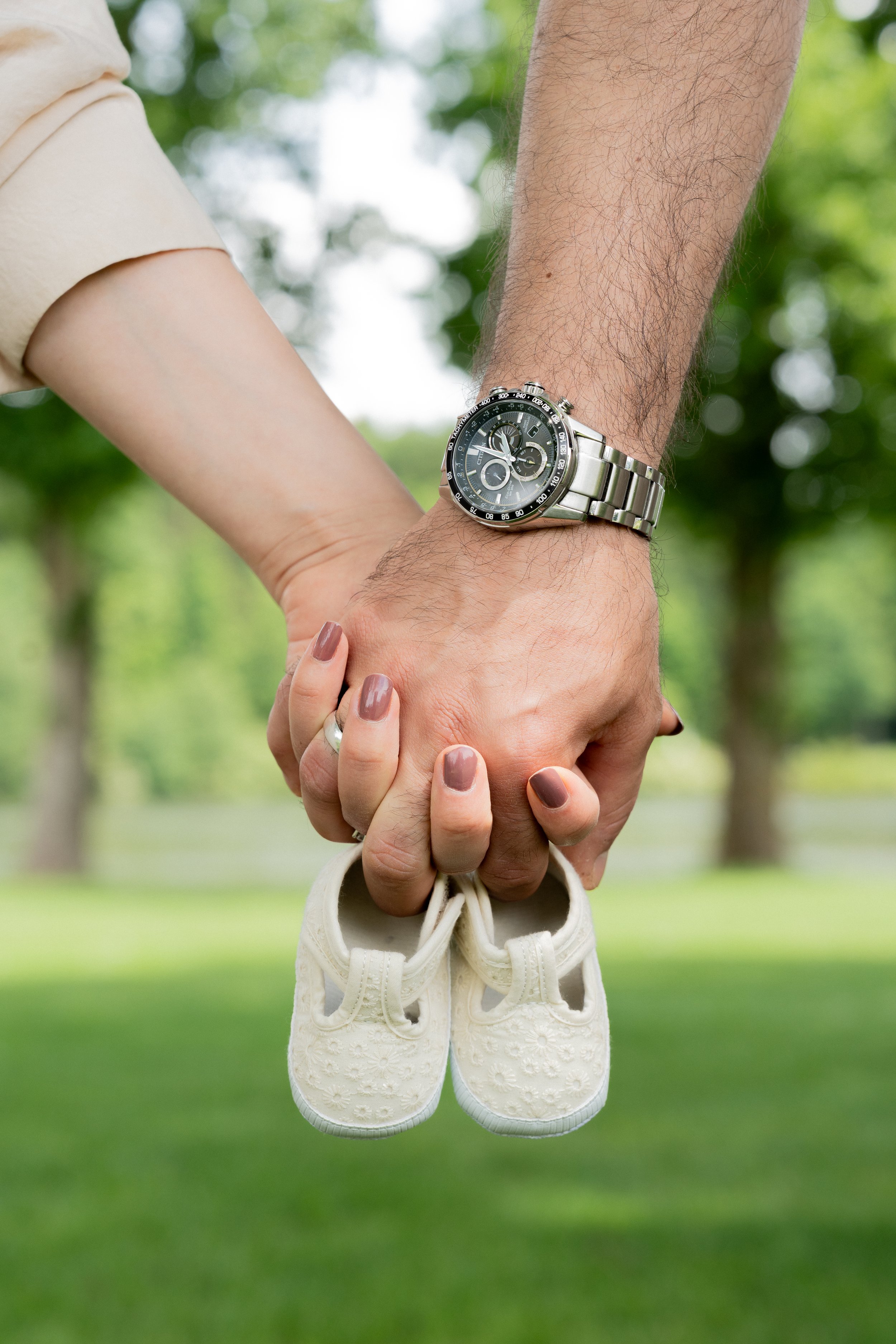 Zwei Menschen halten sich an den Händen, während sie einem Babypaar mit weißen Schnürschuhen im Park eine Freude machen.