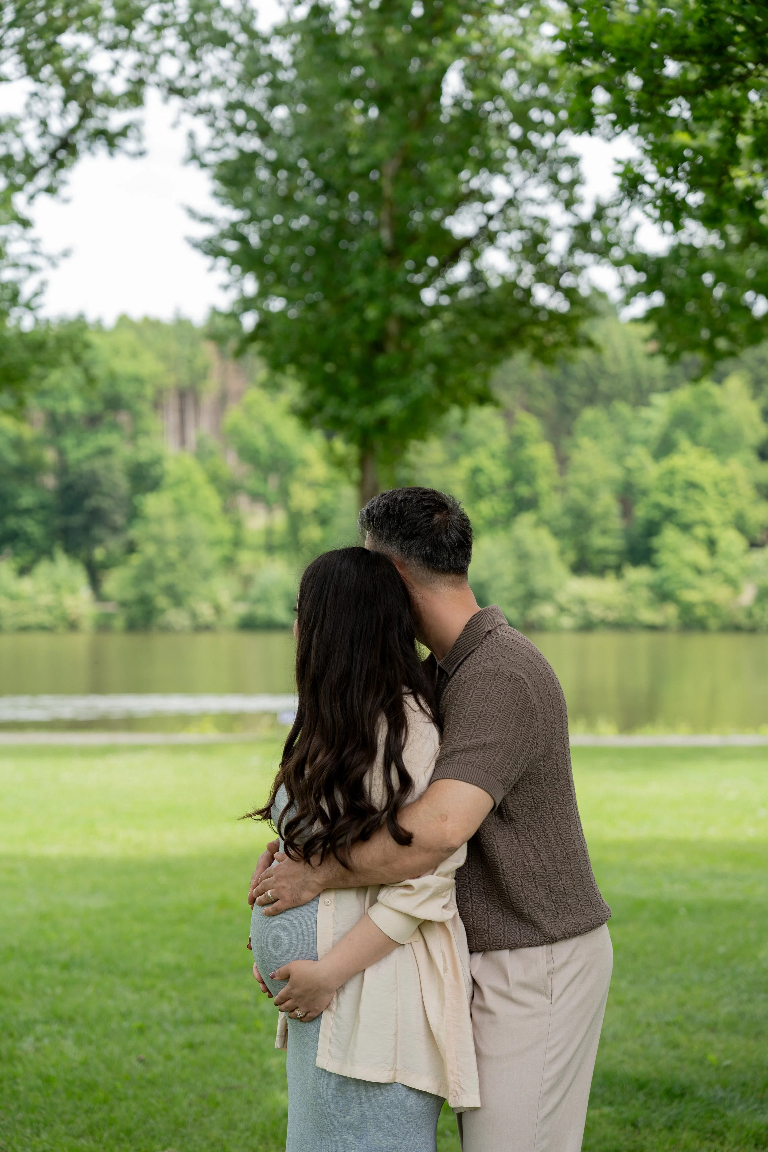 Ein schwangerer Frau und ein Mann, die sich im Park umarmen.