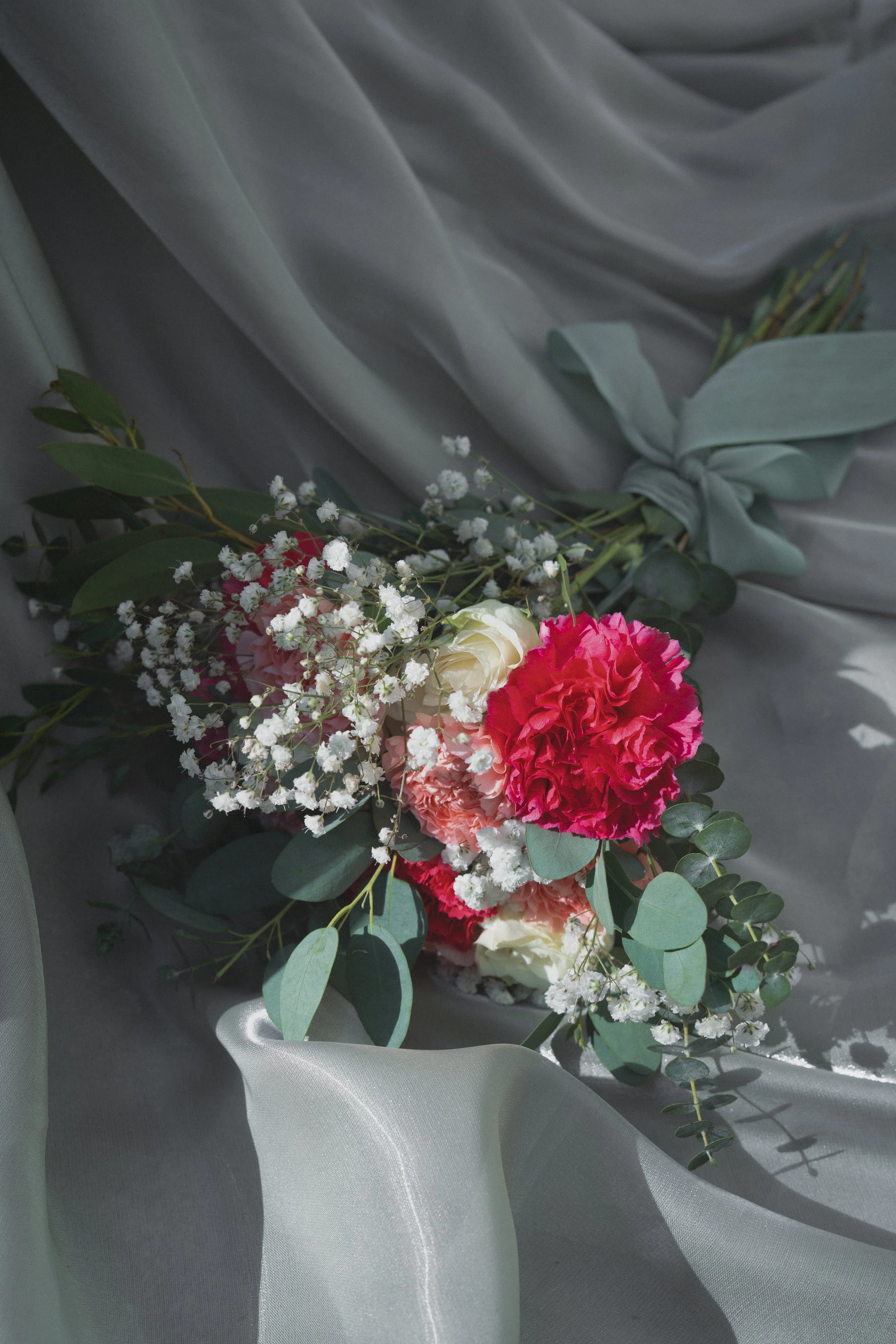 Blumenstrauß aus roten und weißen Blumen mit grünen Blättern, liegend auf glitzerndem, transparentem Stoff