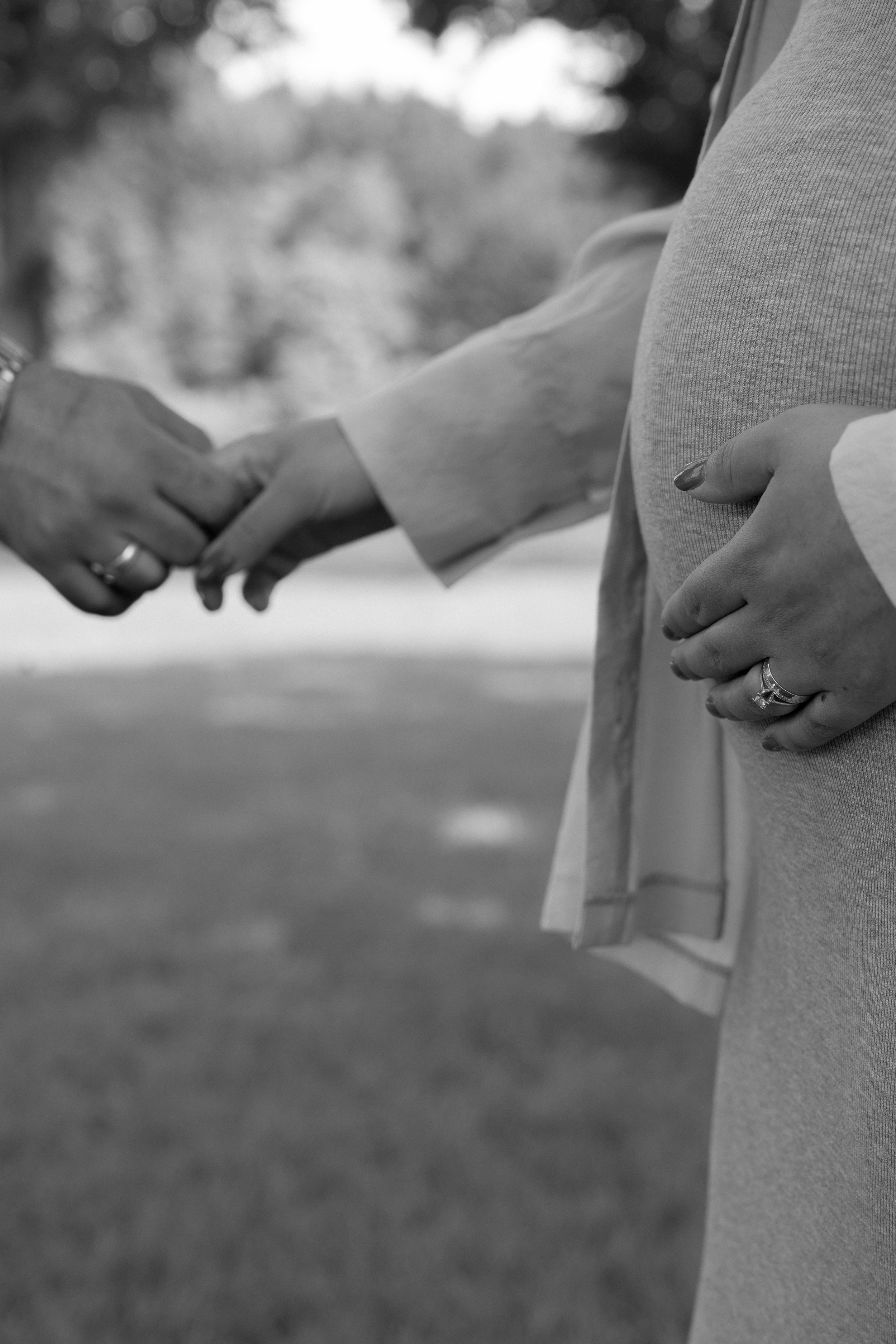 Zwei Menschen halten sich an den Händen, eine Person trägt einen Ehering, das Bild ist in Schwarzweiß.