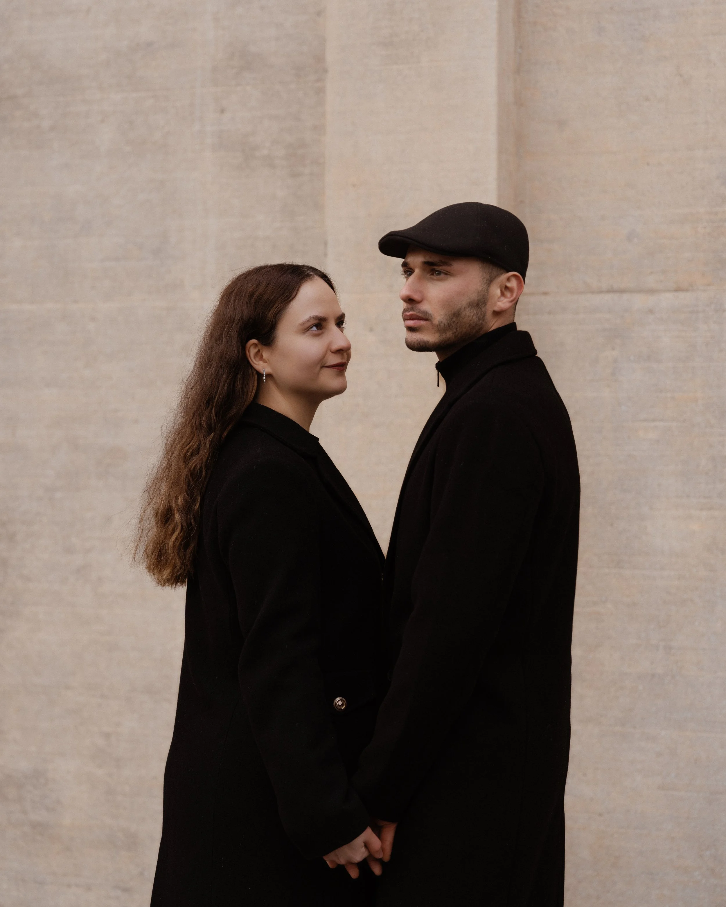 Ein Mann und eine Frau stehen sich gegenüber und halten sich an den Händen vor einer hellen Steinmauer.