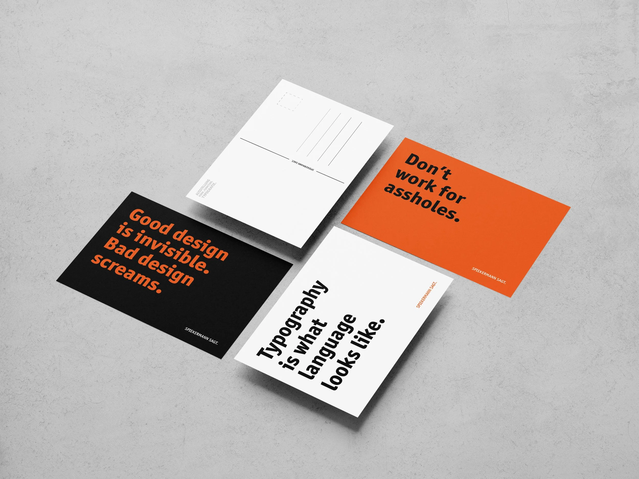Vier Postkarten mit Designzitaten liegen auf einer hellen Oberfläche. Eine Postkarte ist weiß mit schwarzer Schrift, eine ist orange mit schwarzer Schrift, eine ist schwarz mit orange Schrift und die vierte ist weiß mit schwarzer Schrift.