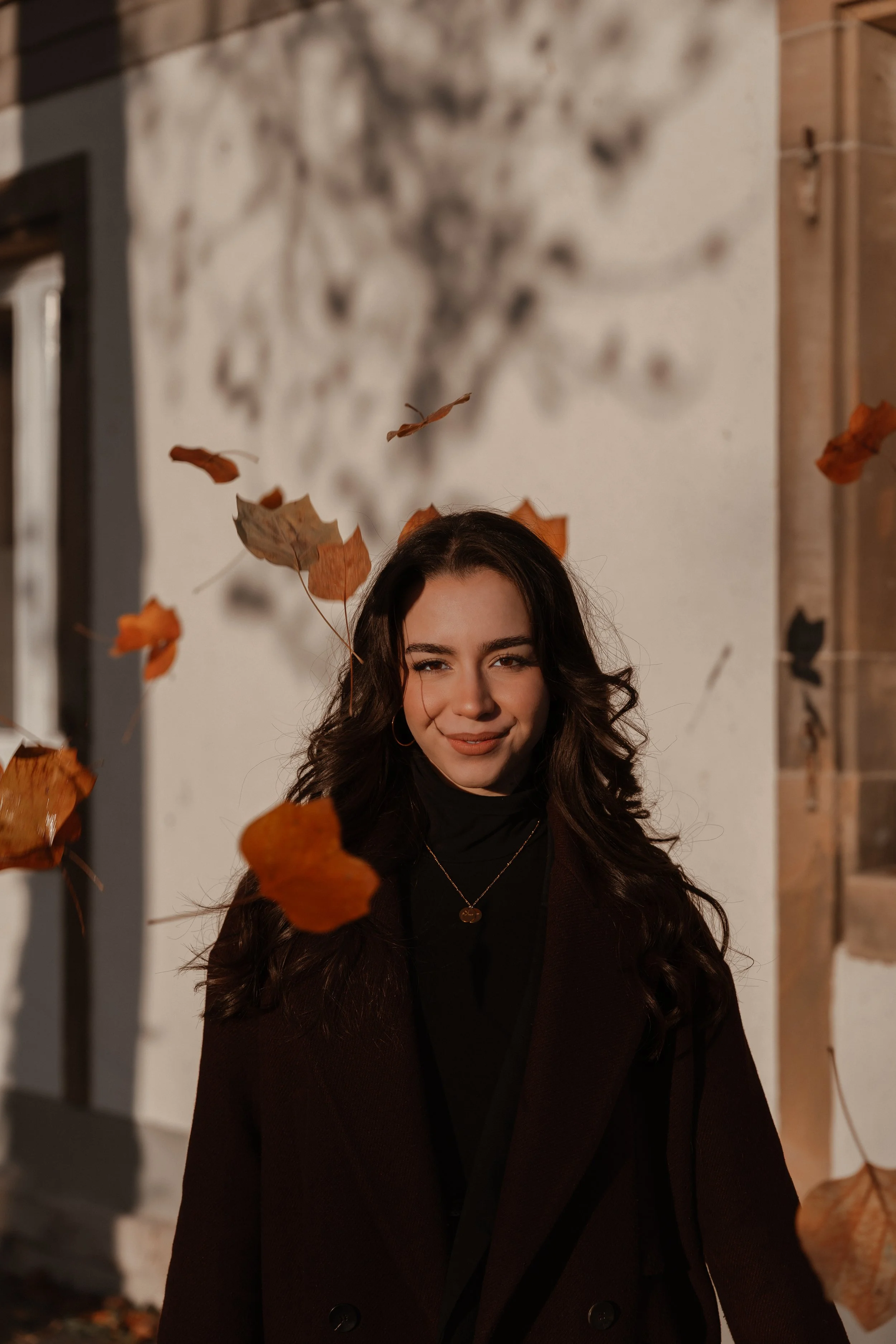 Junge Frau mit dunklen, lockigen Haaren, die im Herbst draußen steht, während Blätter fallen.