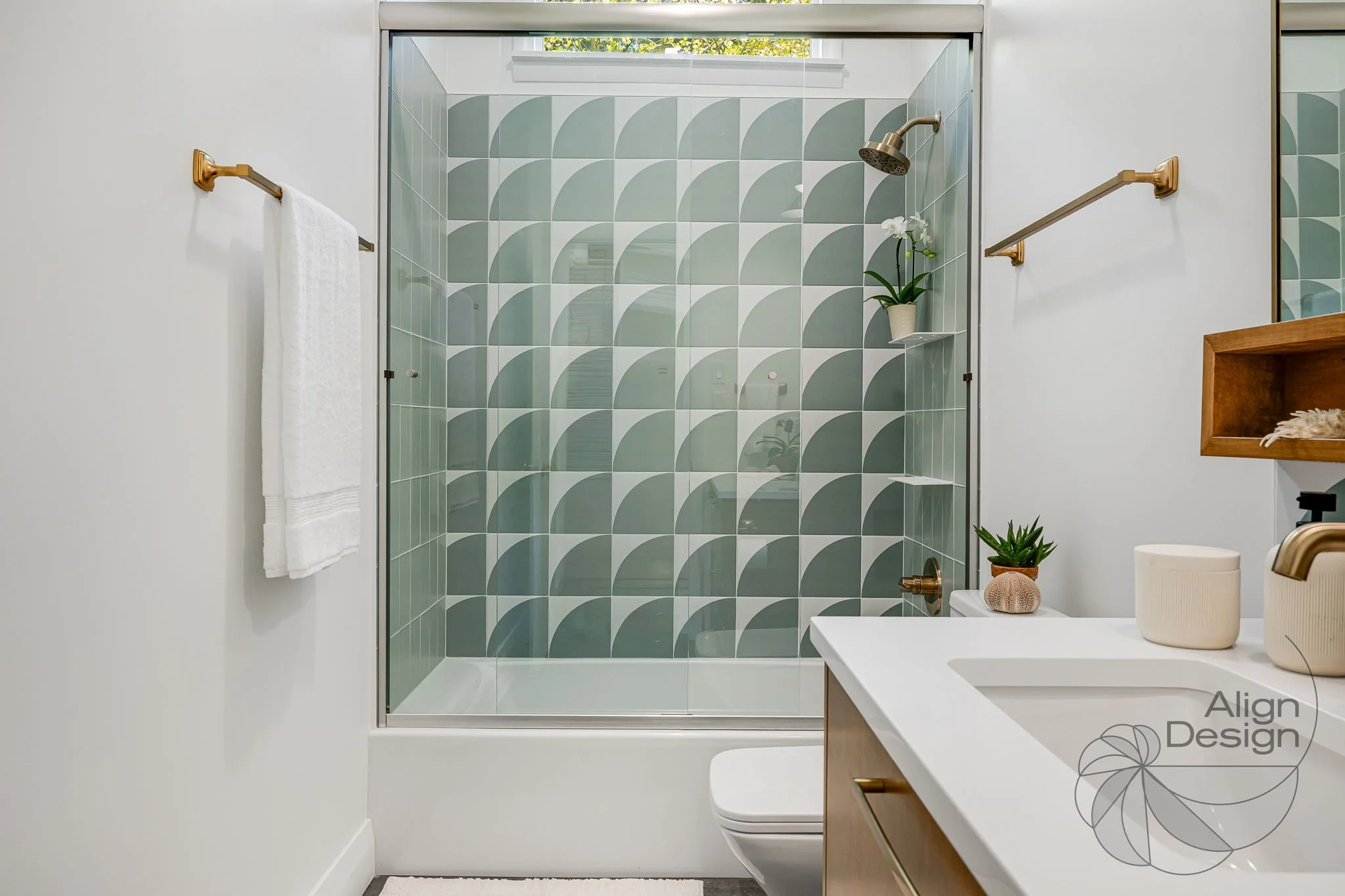 Mid-century modern bathroom with green and white tile, wood vanity, and brass fixtures in a small remodeled space.
