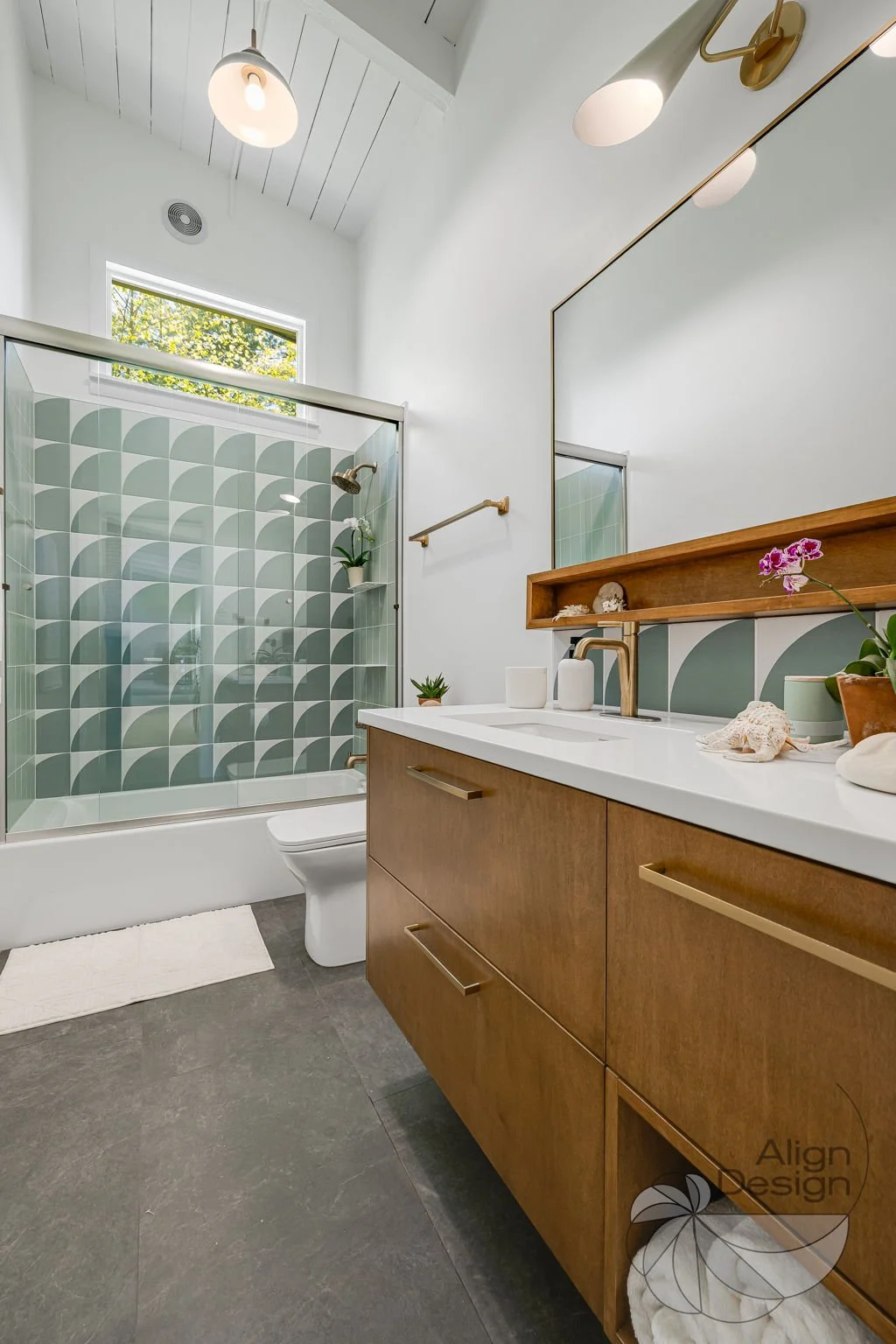 Mid-century modern bathroom with green and white tile, wood vanity, and brass fixtures in a small remodeled space.