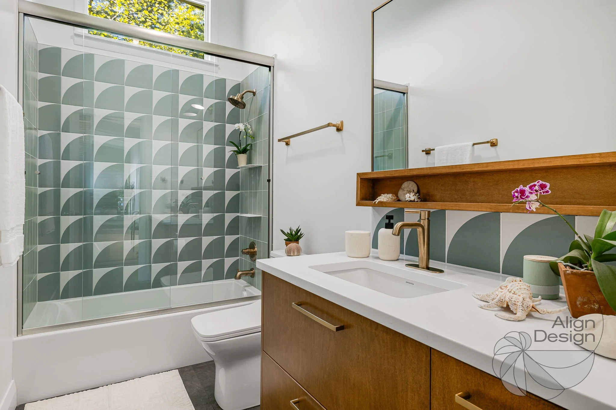 Mid-century modern bathroom with green and white tile, wood vanity, and brass fixtures in a small remodeled space