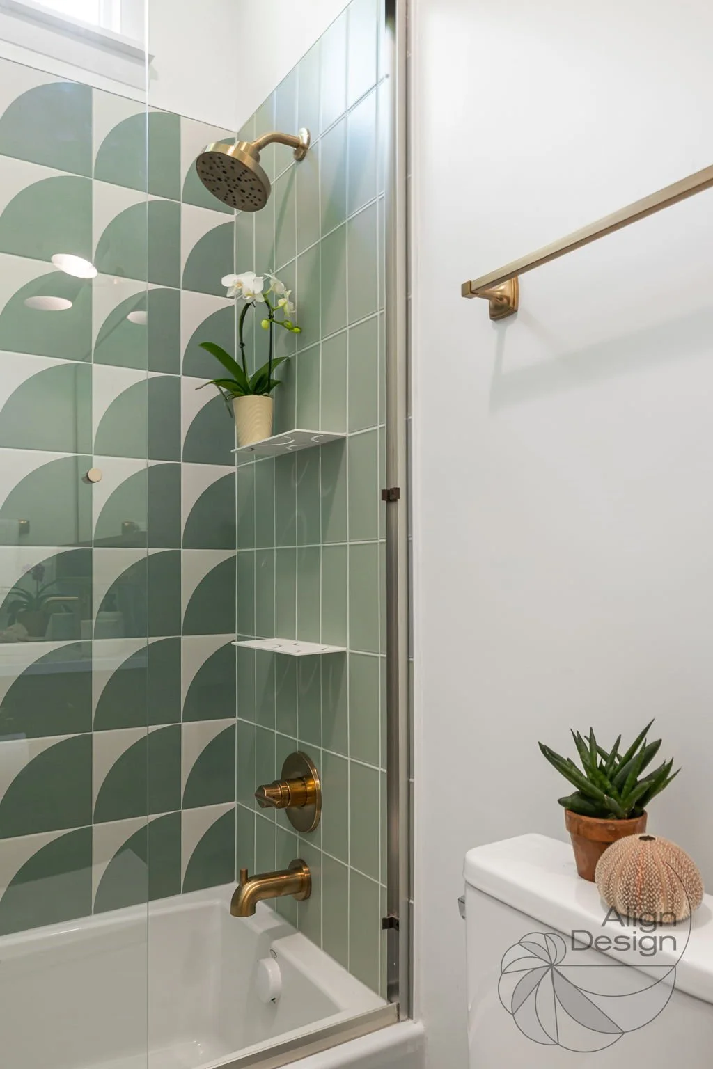 Mid-century modern bathroom with green and white tile, wood vanity, and brass fixtures in a small remodeled space.