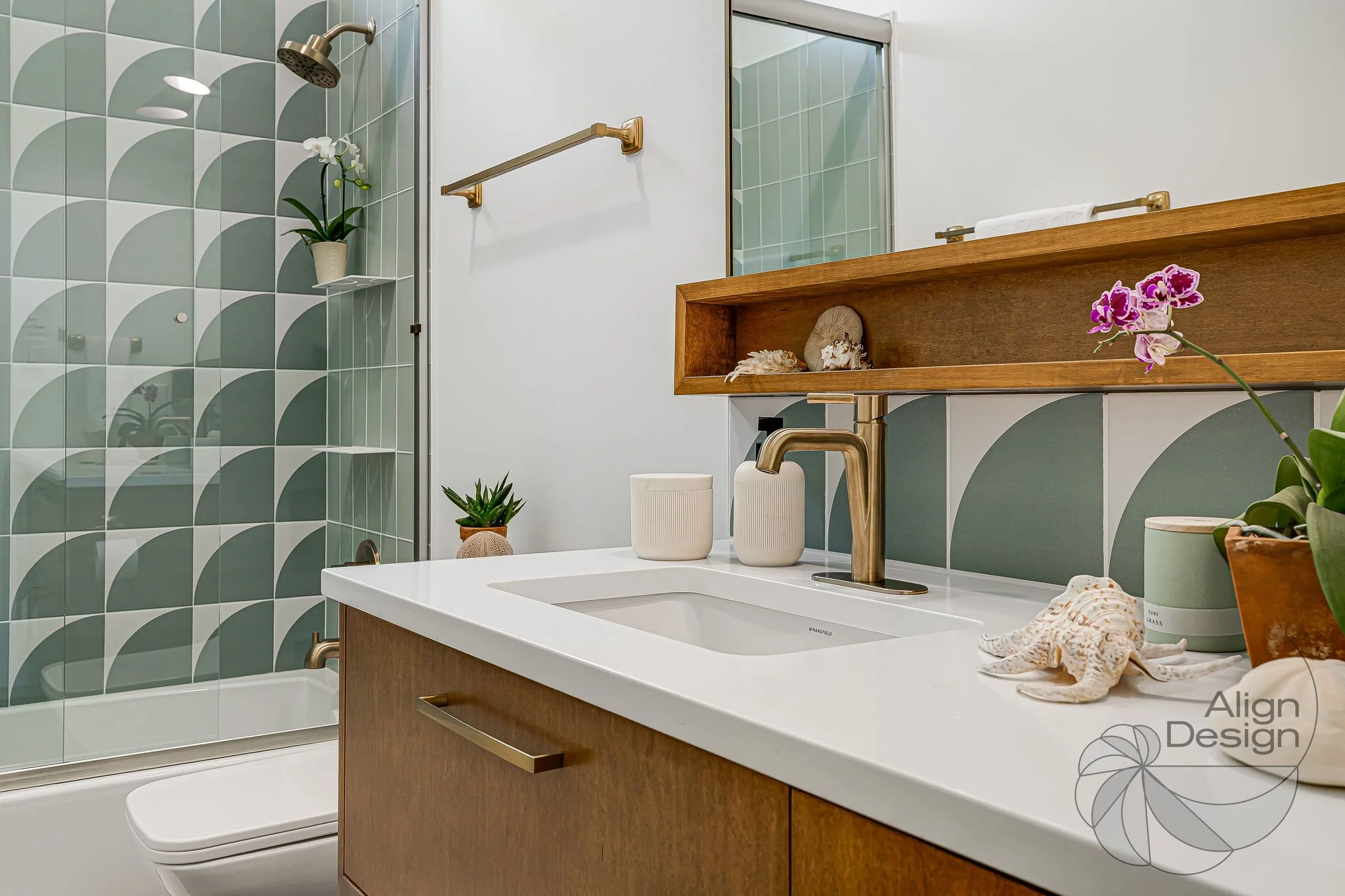 Mid-century modern bathroom with green and white tile, wood vanity, and brass fixtures in a small remodeled space.
