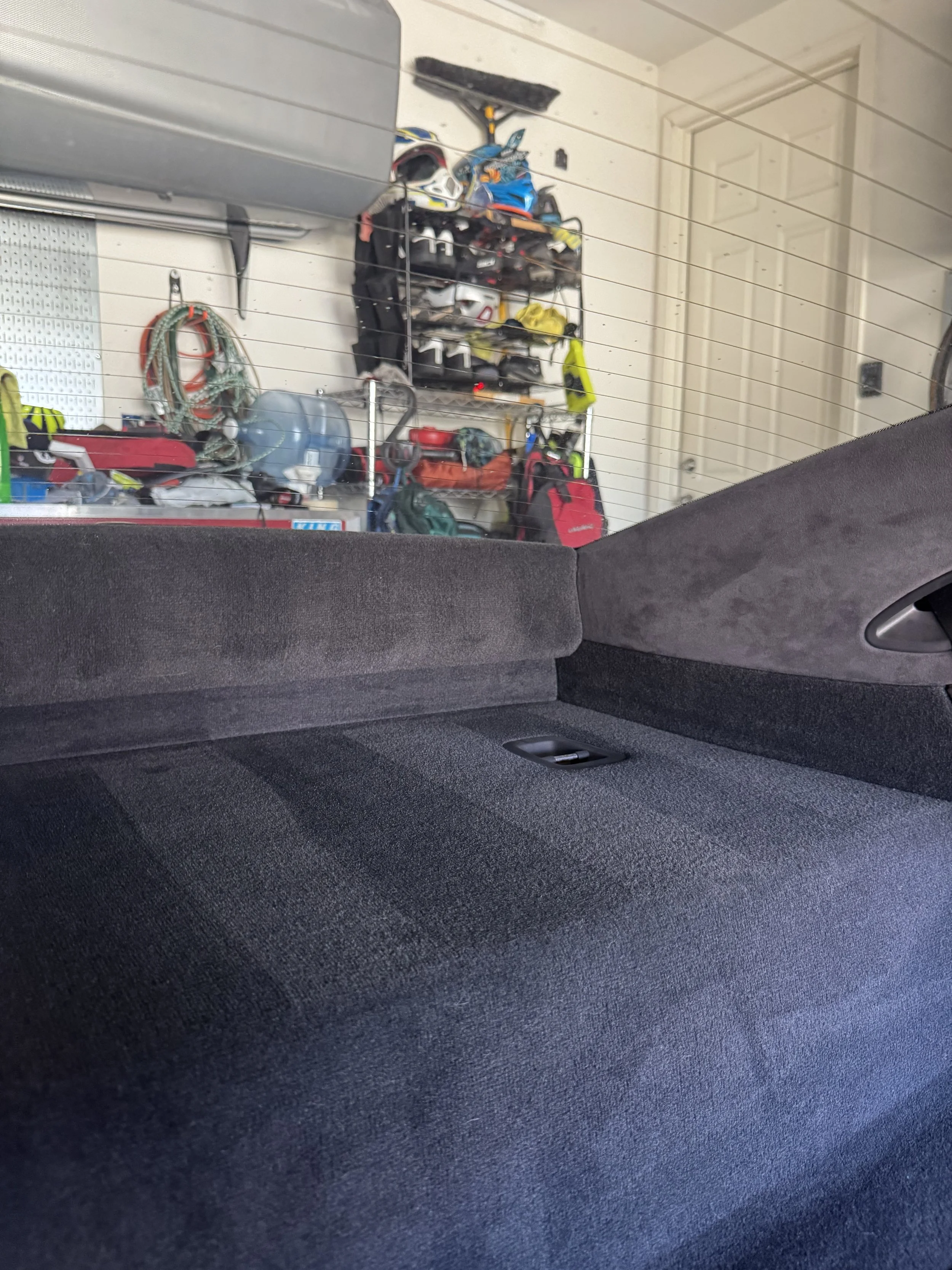 View of the interior of a car trunk with a black fabric lining, showing a garage with tools and equipment on the wall in the background.