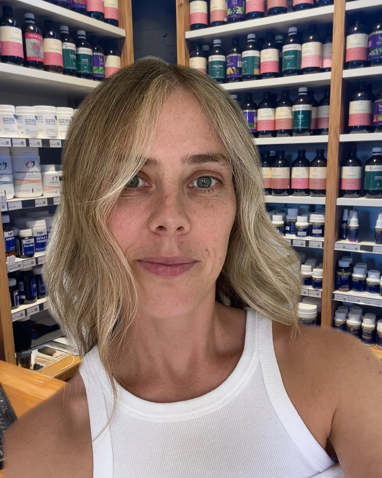 A woman taking a selfie in a health supplement store with shelves of vitamins and supplements behind her.