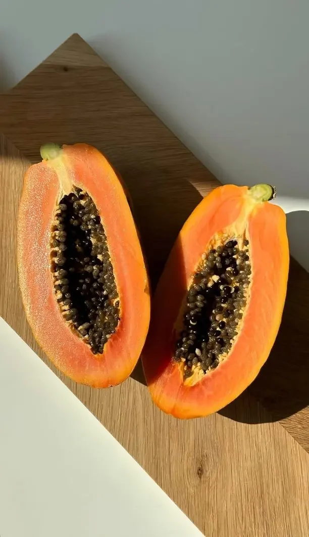 Halved ripe papaya with orange flesh and black seeds on a wooden surface.