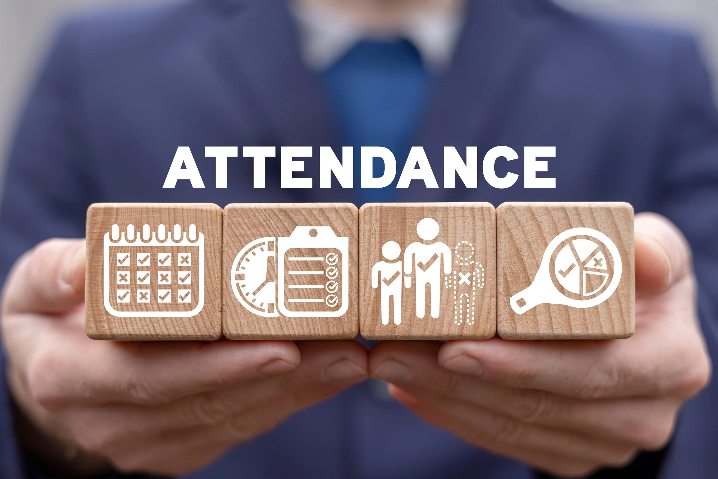 Hand holding four wooden blocks with white icons and text related to attendance, scheduling, and data analysis.
