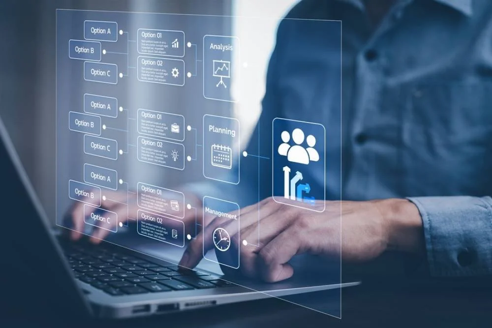 Person using a laptop with a transparent futuristic digital interface displaying flowcharts, icons for analysis, planning, and management.