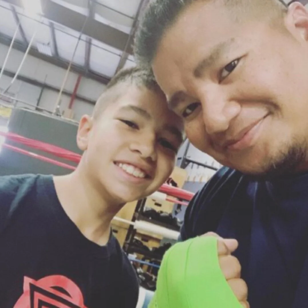 Two people smiling in a gym setting, one with green hand wraps.