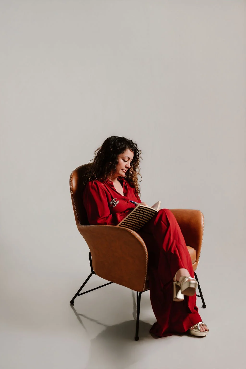 Cynthia Platero, executive coach for high-achieving creative women sitting in a brown chair, writing in a notebook.