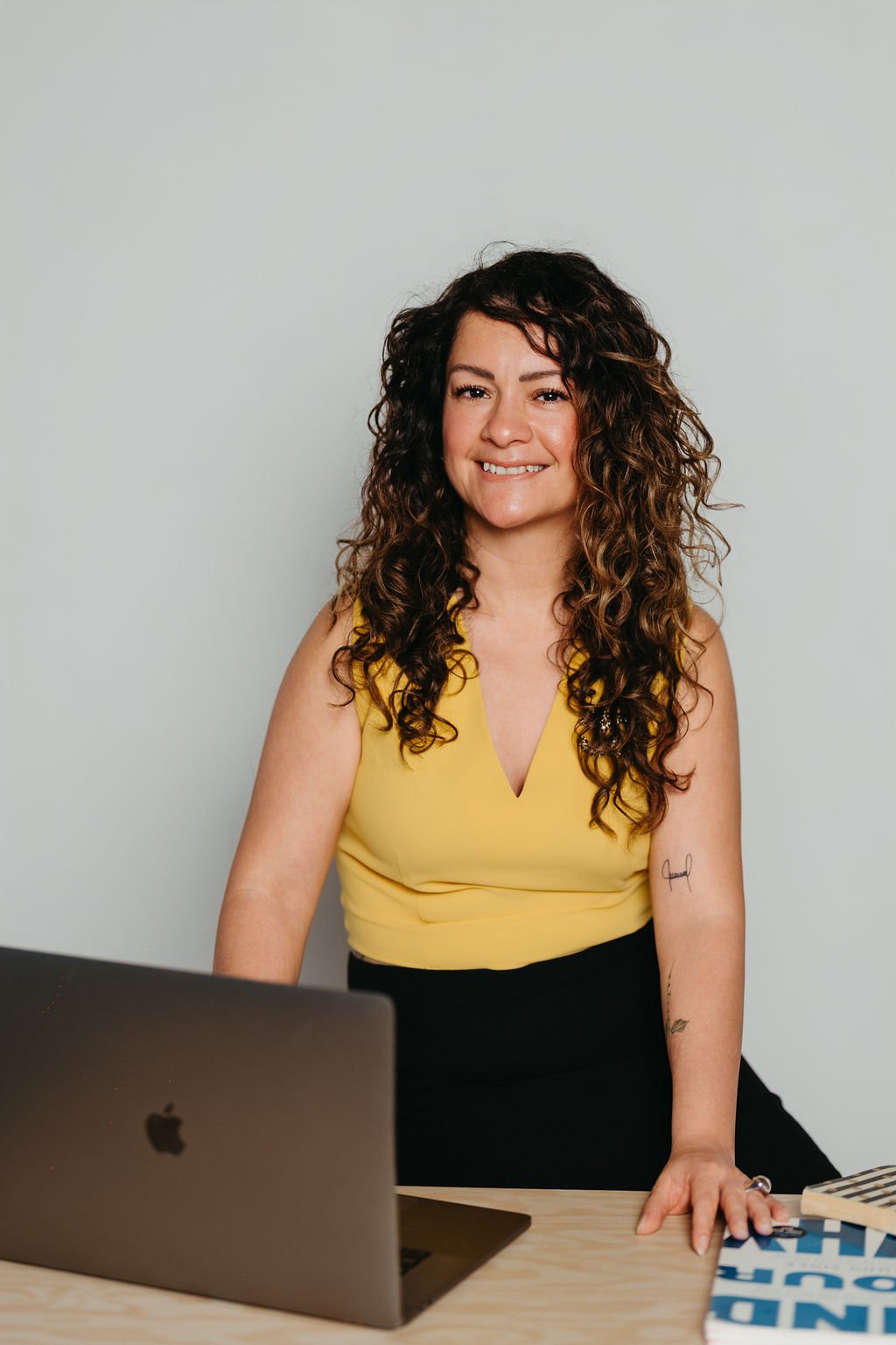 Cynthia Platero, executive coach for high-achieving creative women sitting behind a desk with a laptop and book.