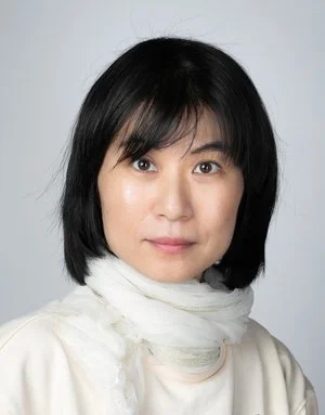 Portrait of a woman with short black hair wearing a white scarf around her neck, looking at the camera.