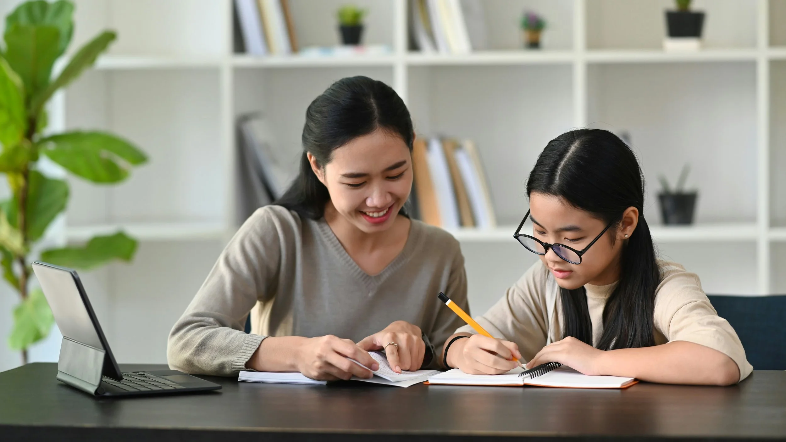An adult tutor guides a student working in a notebook during a one-on-one study session.