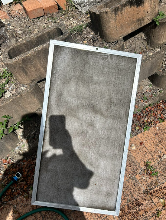 Dirty air filter leaning against cinder blocks outdoors with a garden hose nearby.