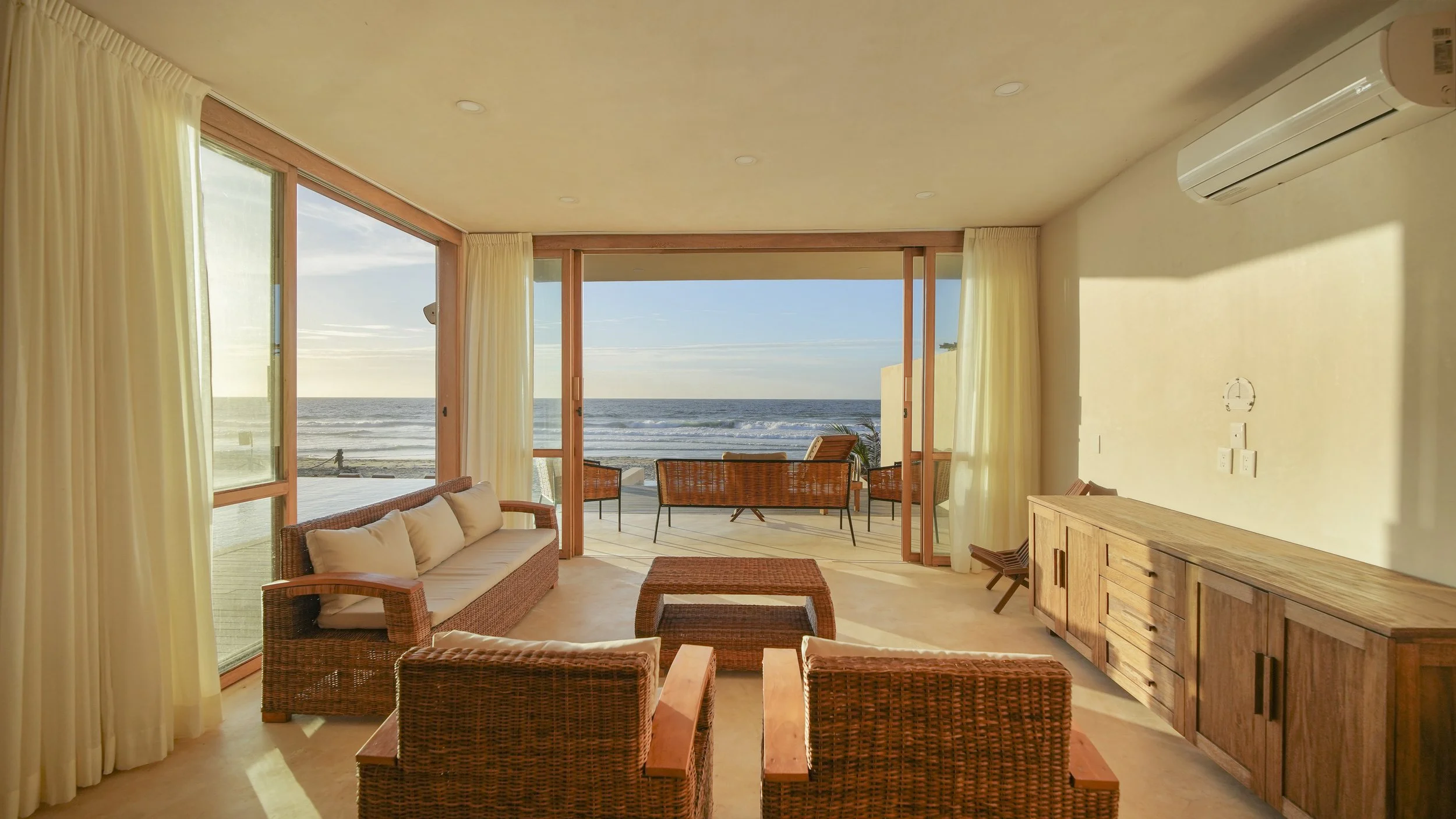 Living room with wicker furniture and a view of the ocean through large glass doors.